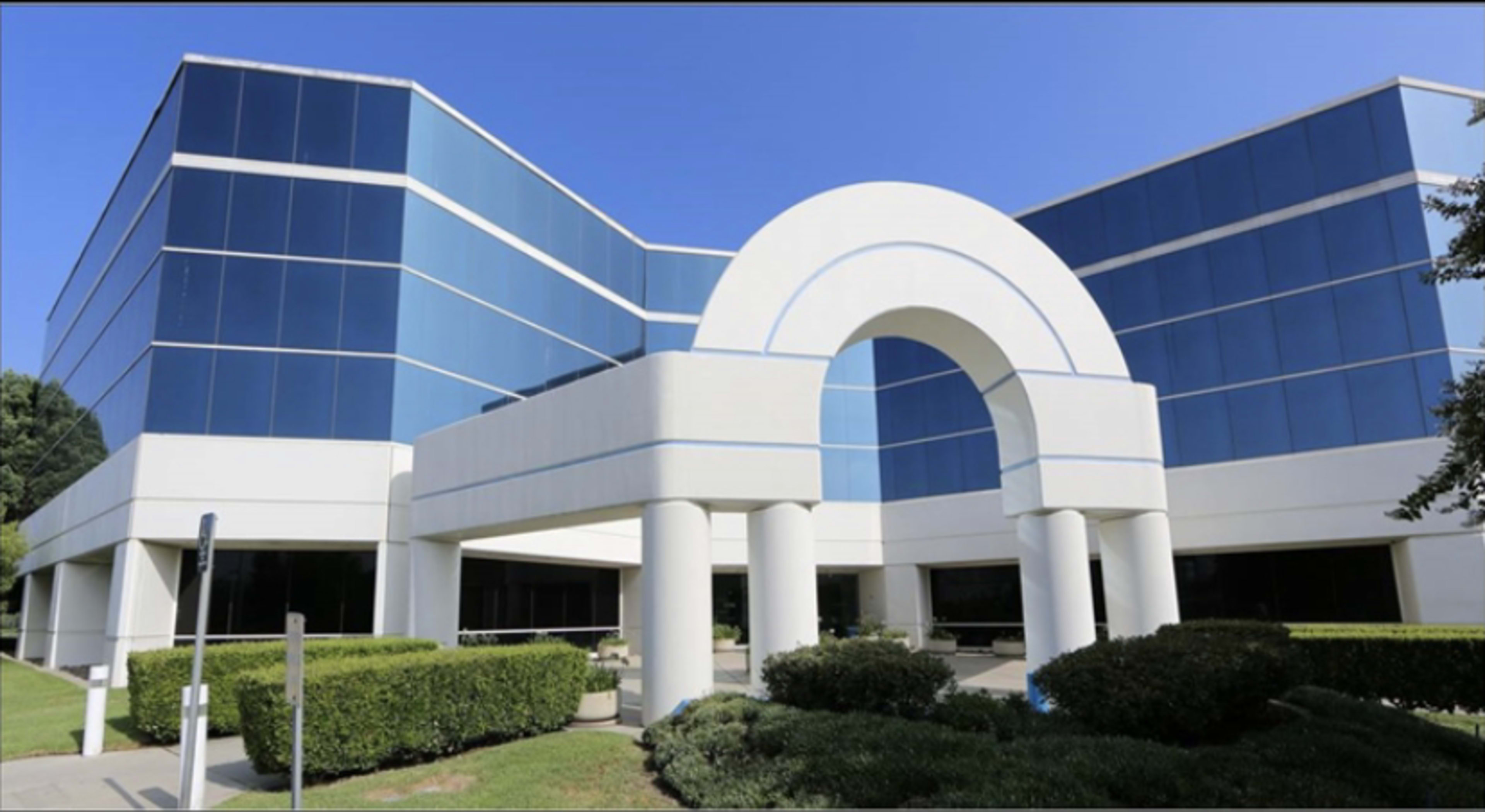 The building features a modern design with large blue glass windows and a prominent white arch entrance supported by columns.