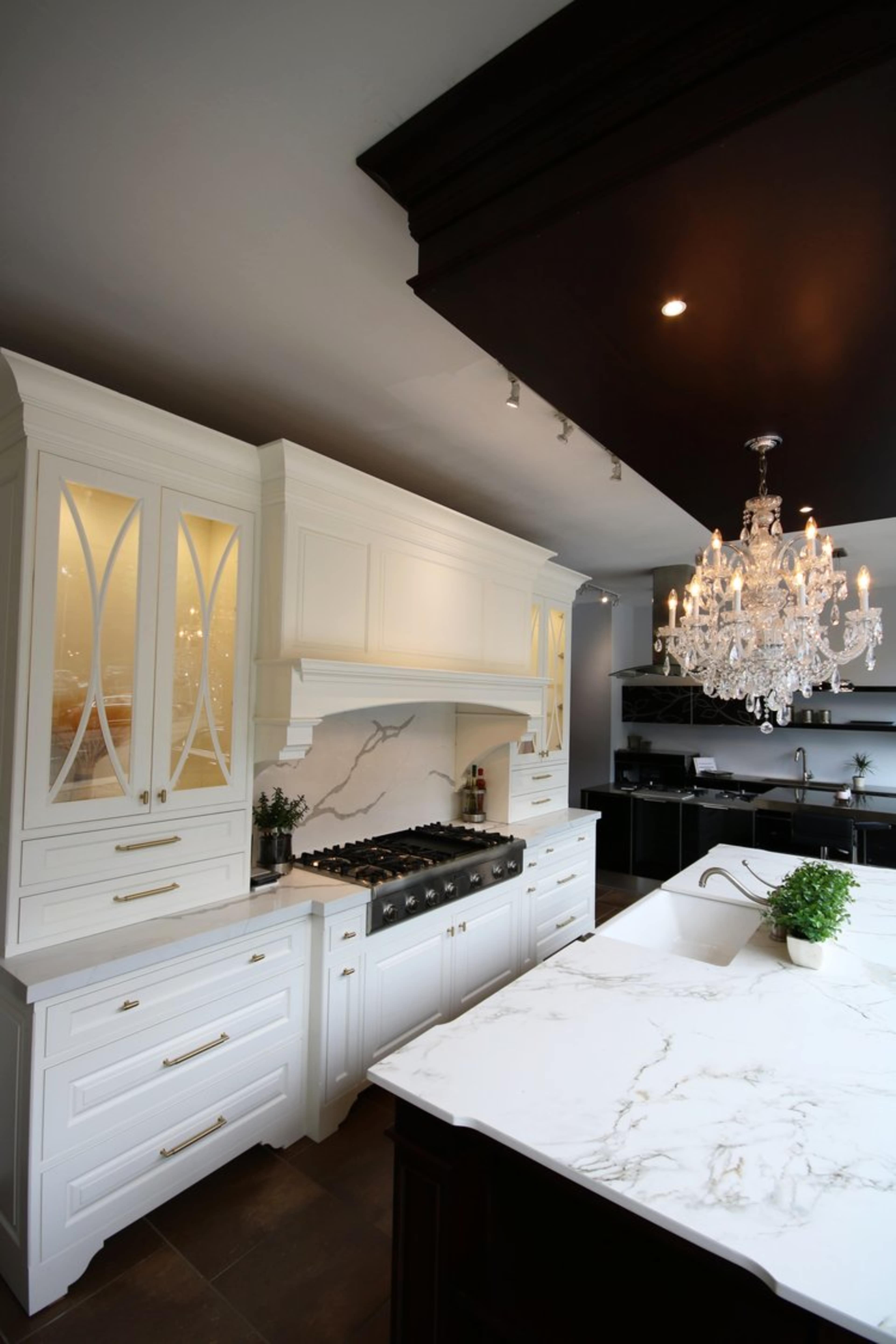 A modern kitchen features white cabinetry, a marble countertop, and a large chandelier overhead.
