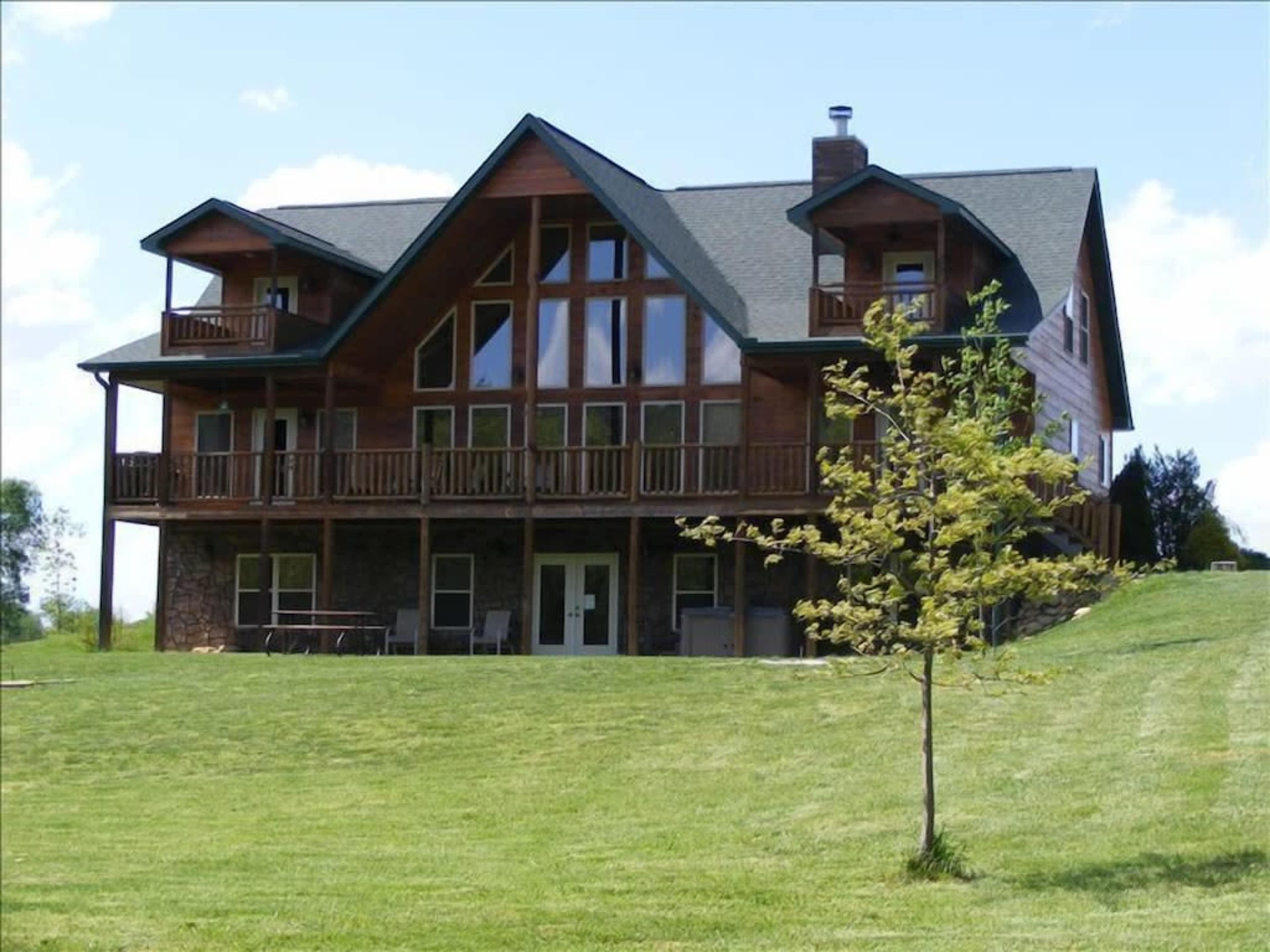A large two-story wooden house with a peaked roof and multiple balconies overlooks a green lawn under a clear blue sky.
