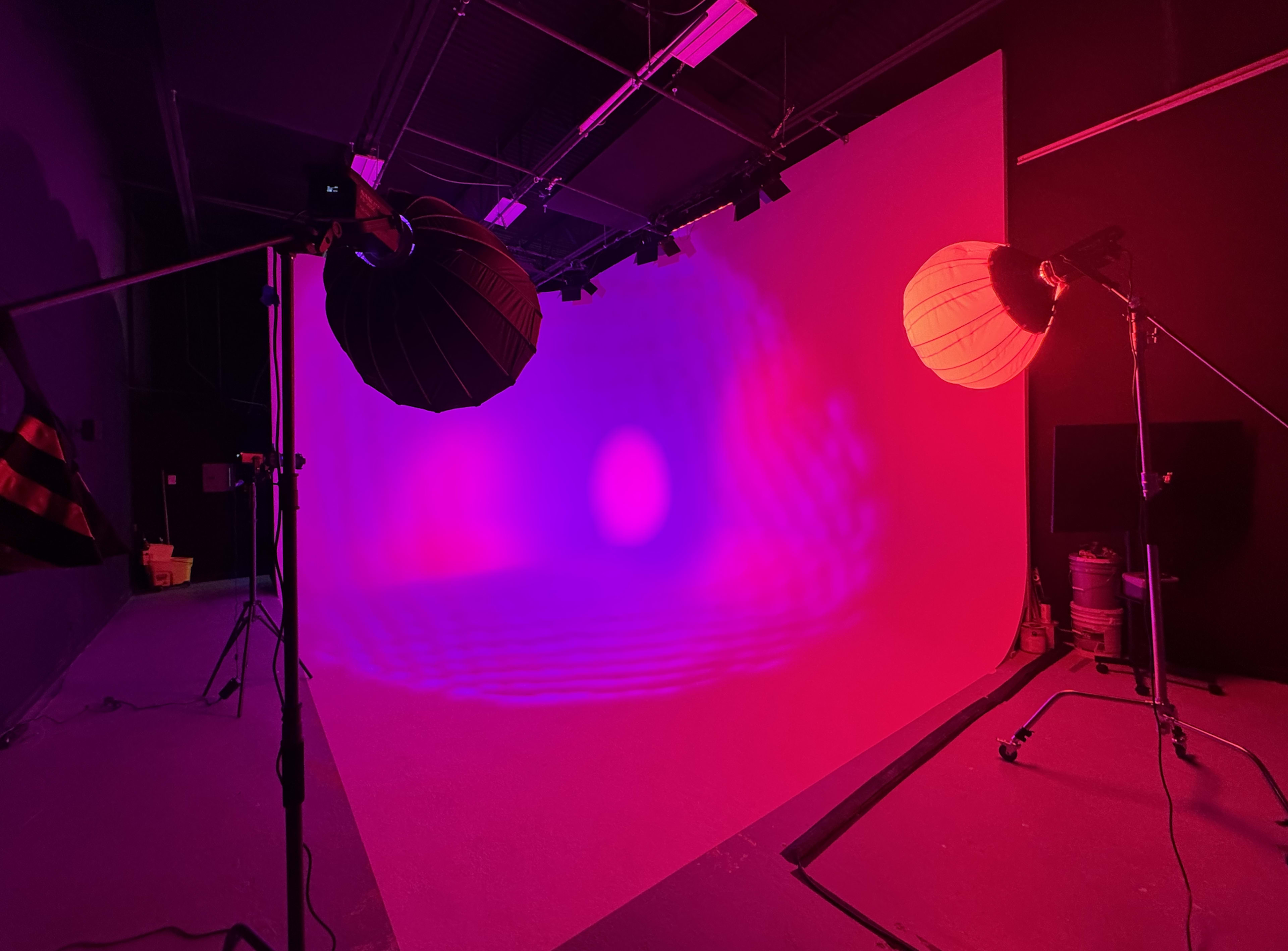 The image shows a photography studio with a white backdrop illuminated by colorful lighting from two softbox lamps.