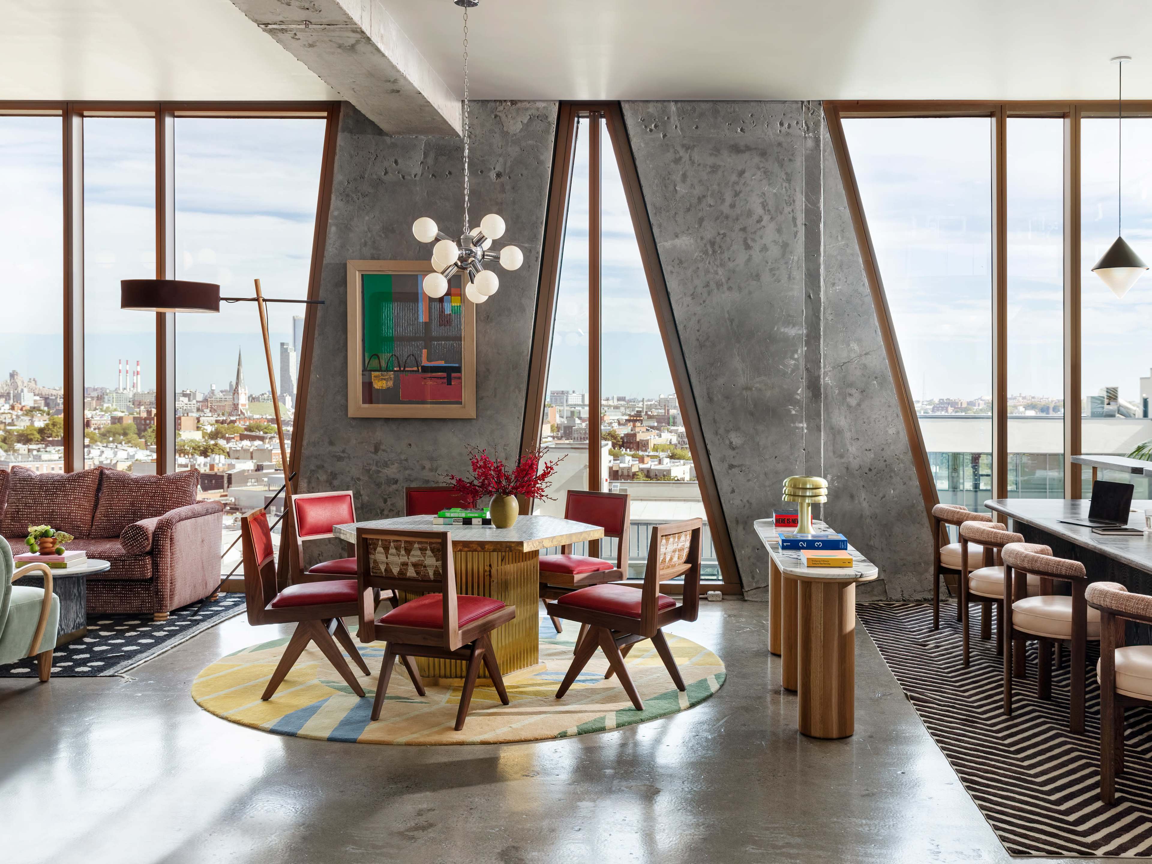 A modern dining area with a geometric rug, a round dining table surrounded by wooden chairs, and large windows offering a view of a city skyline.