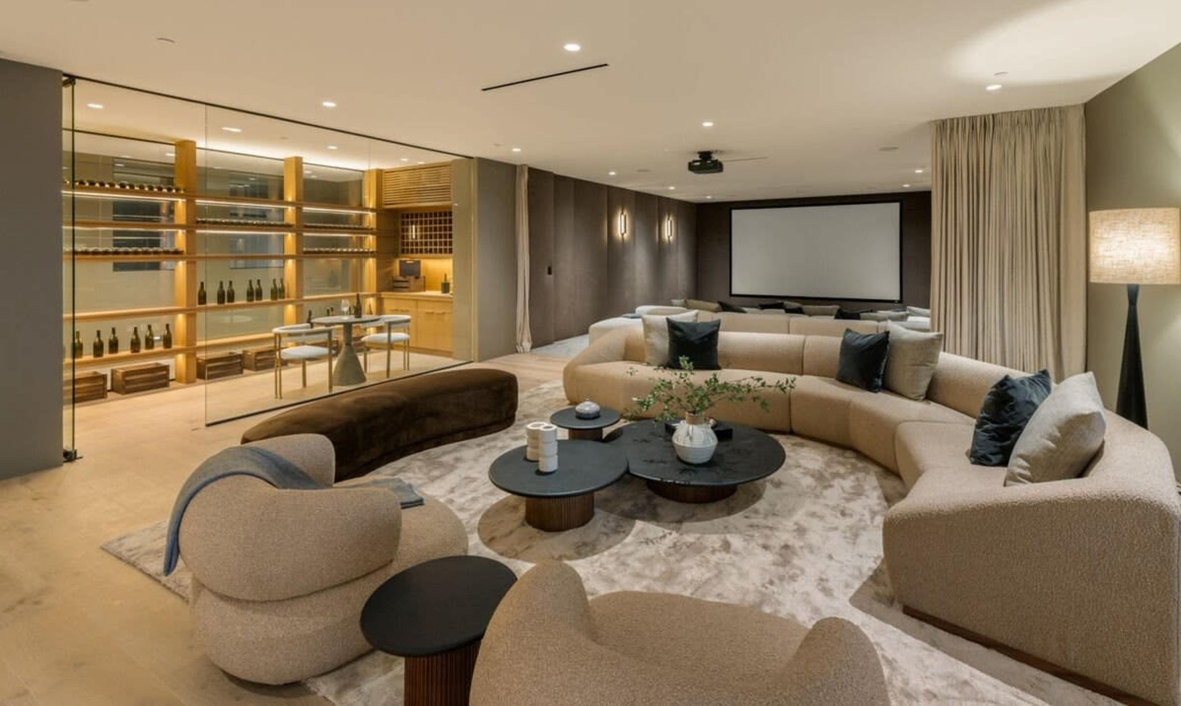 The image shows a modern living room with a large curved sofa, a round coffee table, and a separate dining area visible in the background.