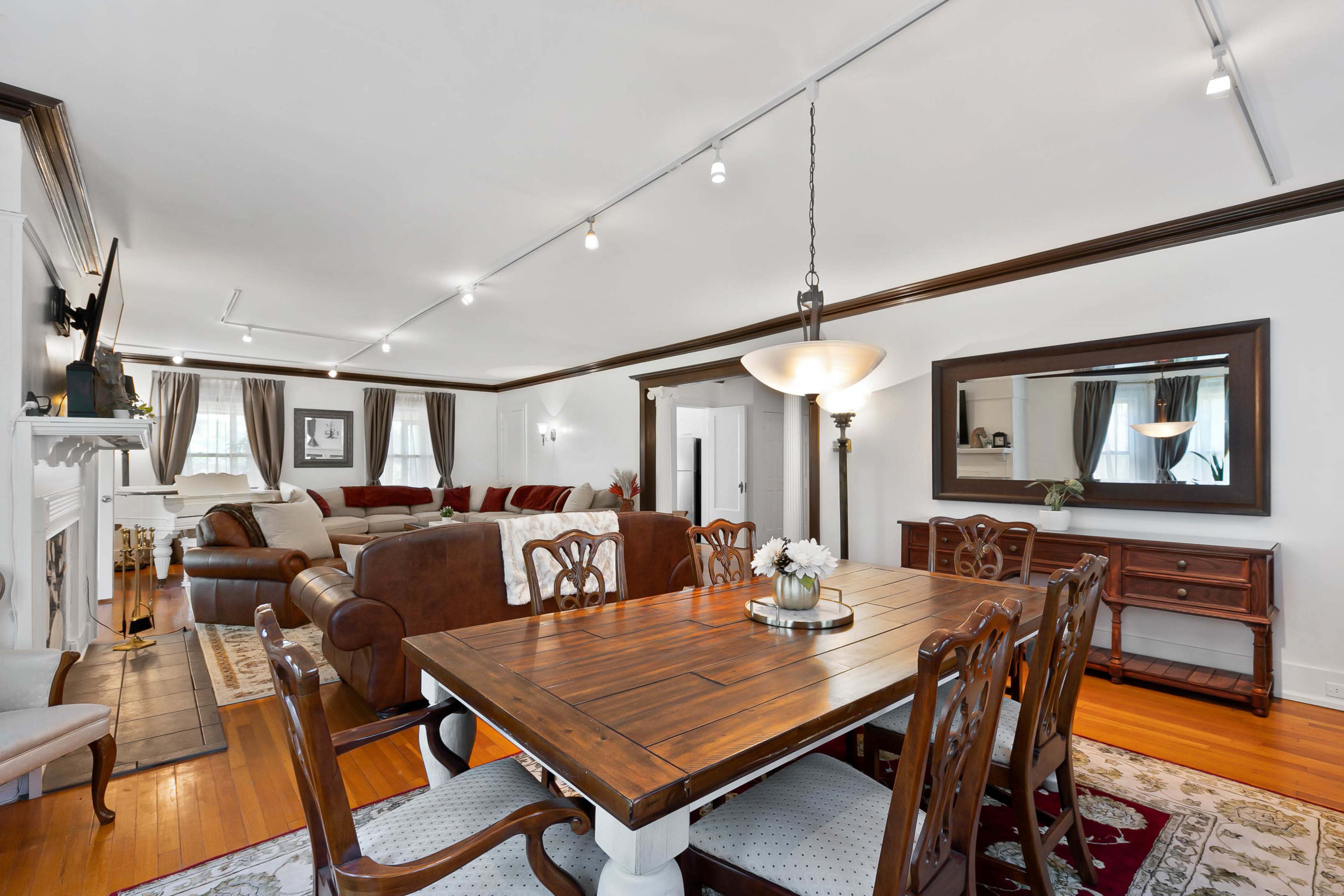 A spacious living and dining area features a wooden dining table surrounded by upholstered chairs, with a sectional sofa and a fireplace in the background.