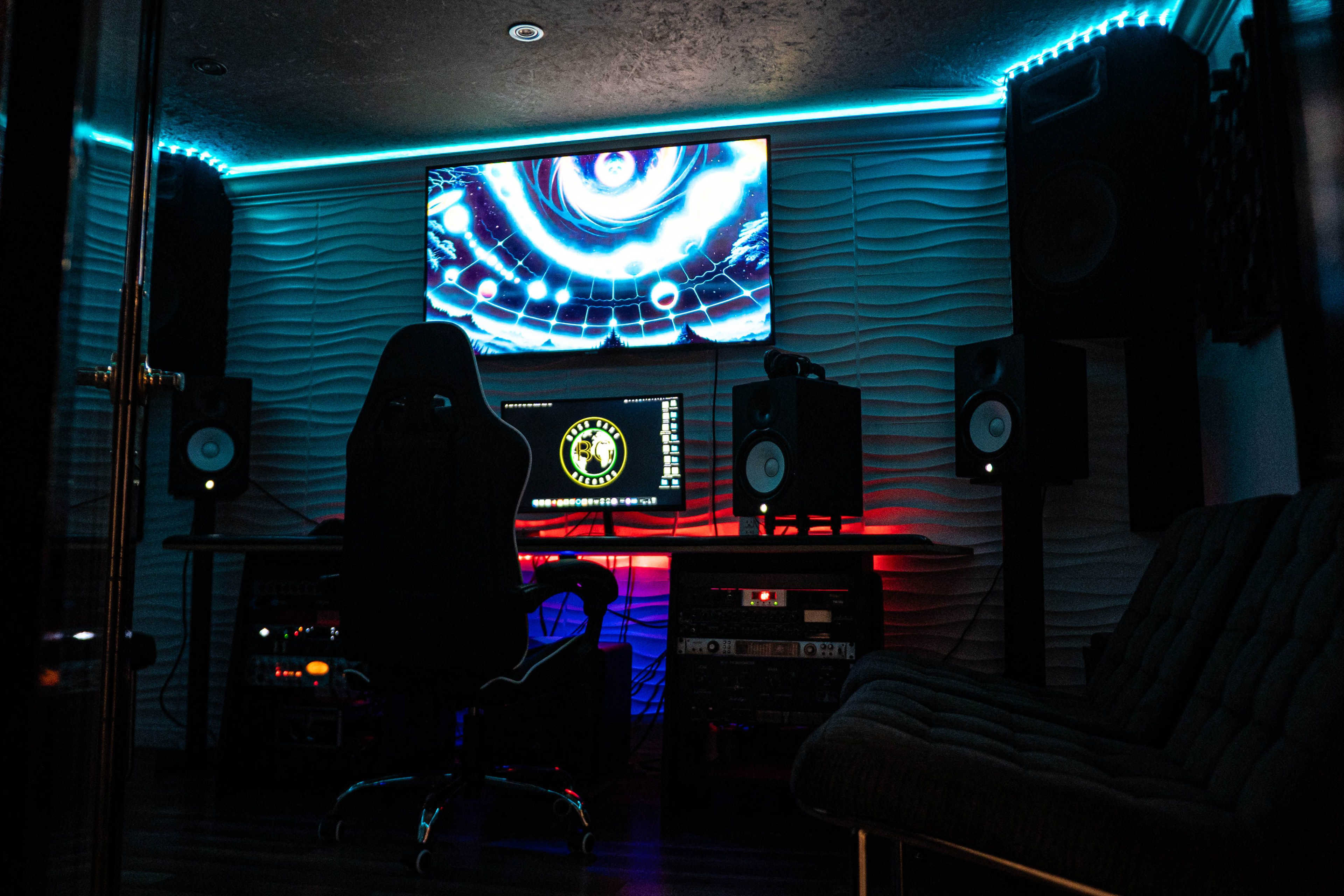 The image shows a modern music studio with a centralized desk, computer monitors, speakers, and ambient LED lighting.