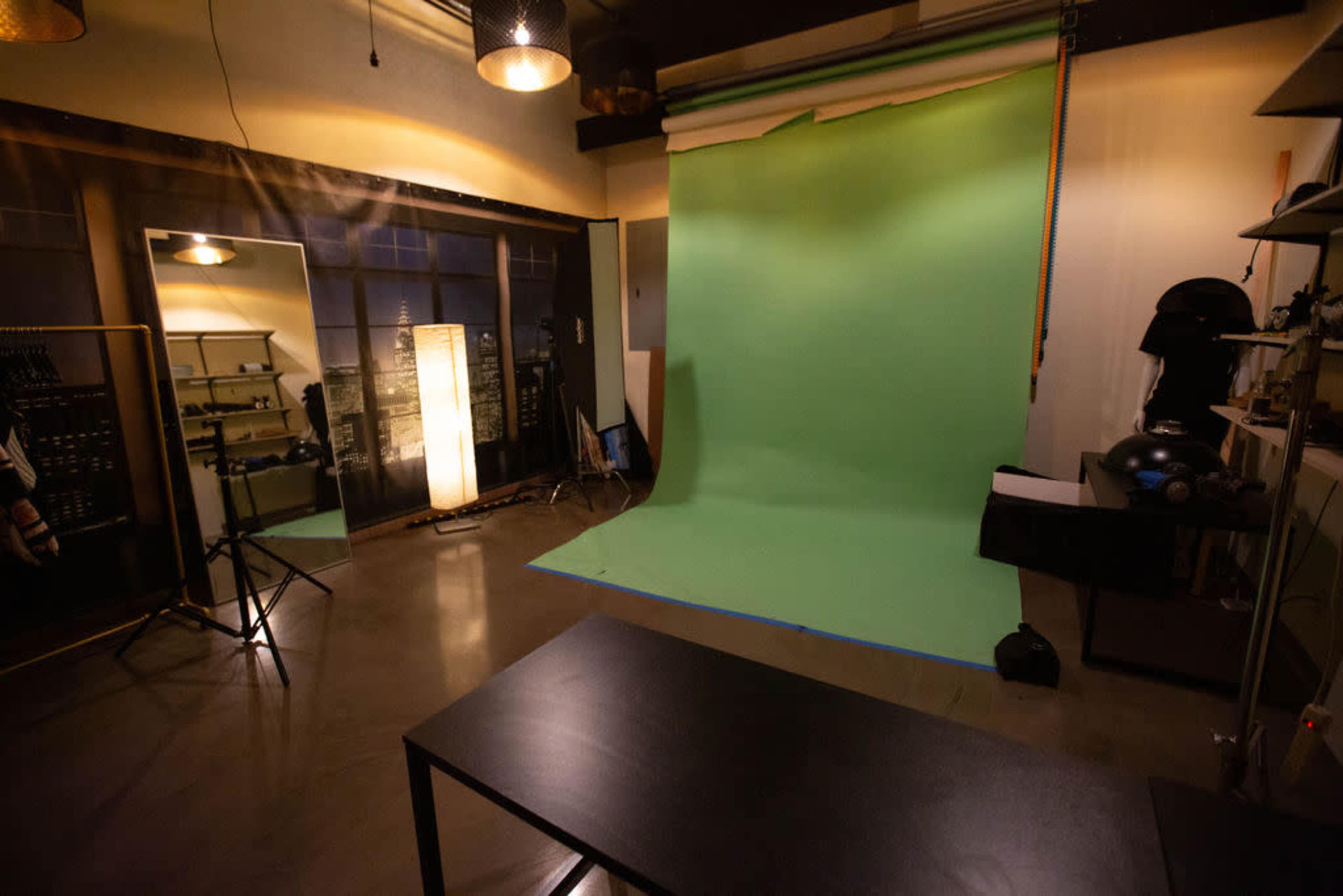 The image shows a photography studio featuring a green screen backdrop, a large mirror, soft lighting, and various equipment arranged in the space.