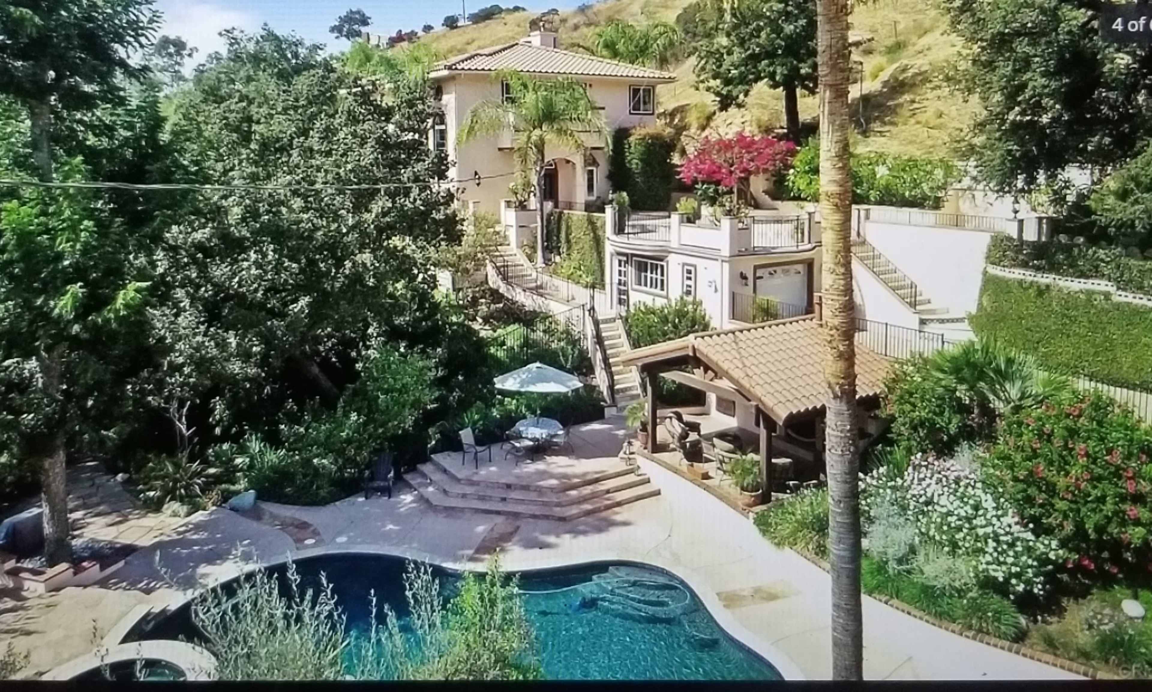 A multi-level home surrounded by lush greenery features a swimming pool and a shaded patio area.