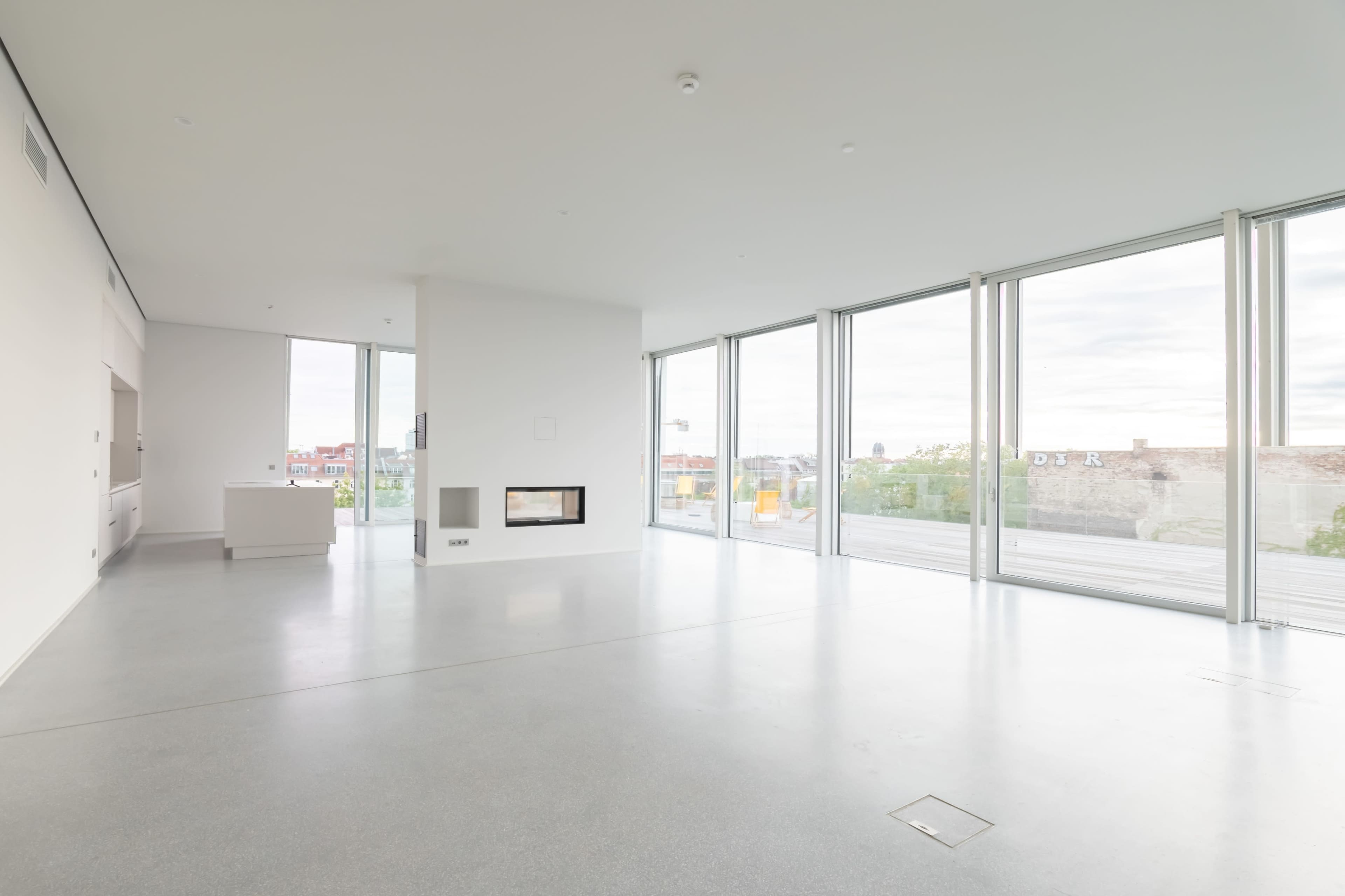 The image shows a spacious, minimalist living room with large floor-to-ceiling windows and a modern fireplace.