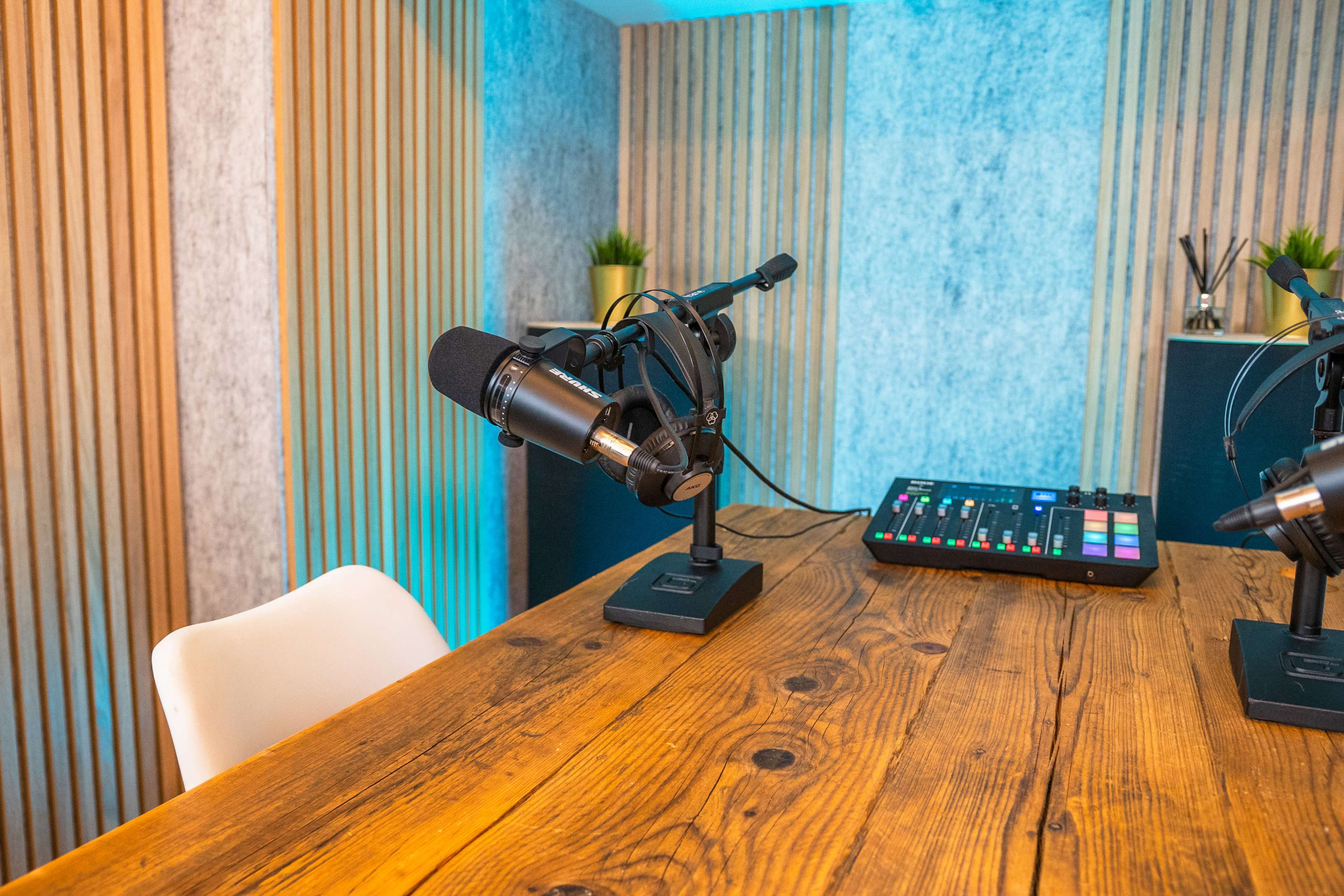 A wooden table with two microphones and a sound mixing console in a studio environment.