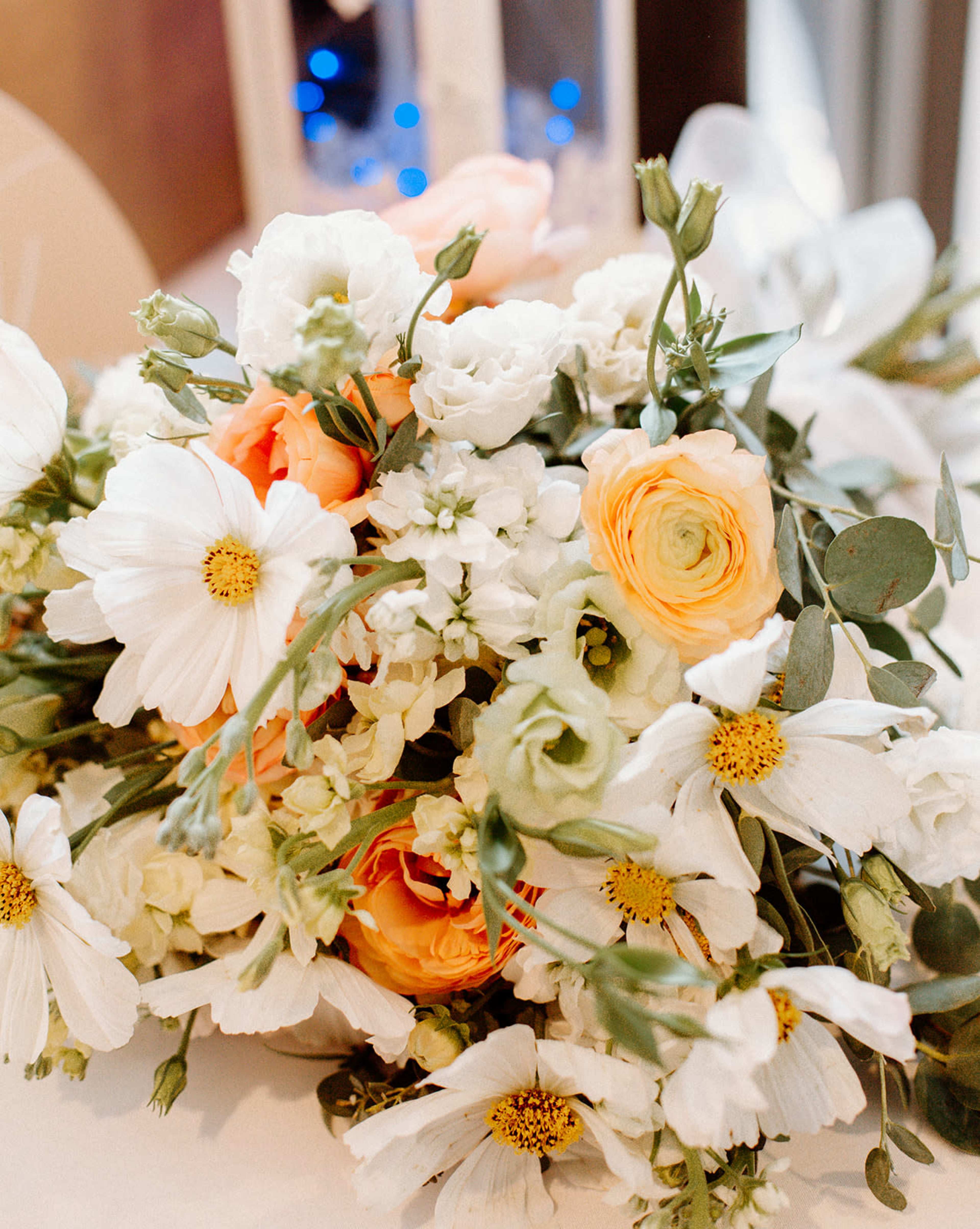 A floral arrangement features white daisies, orange roses, and green foliage.