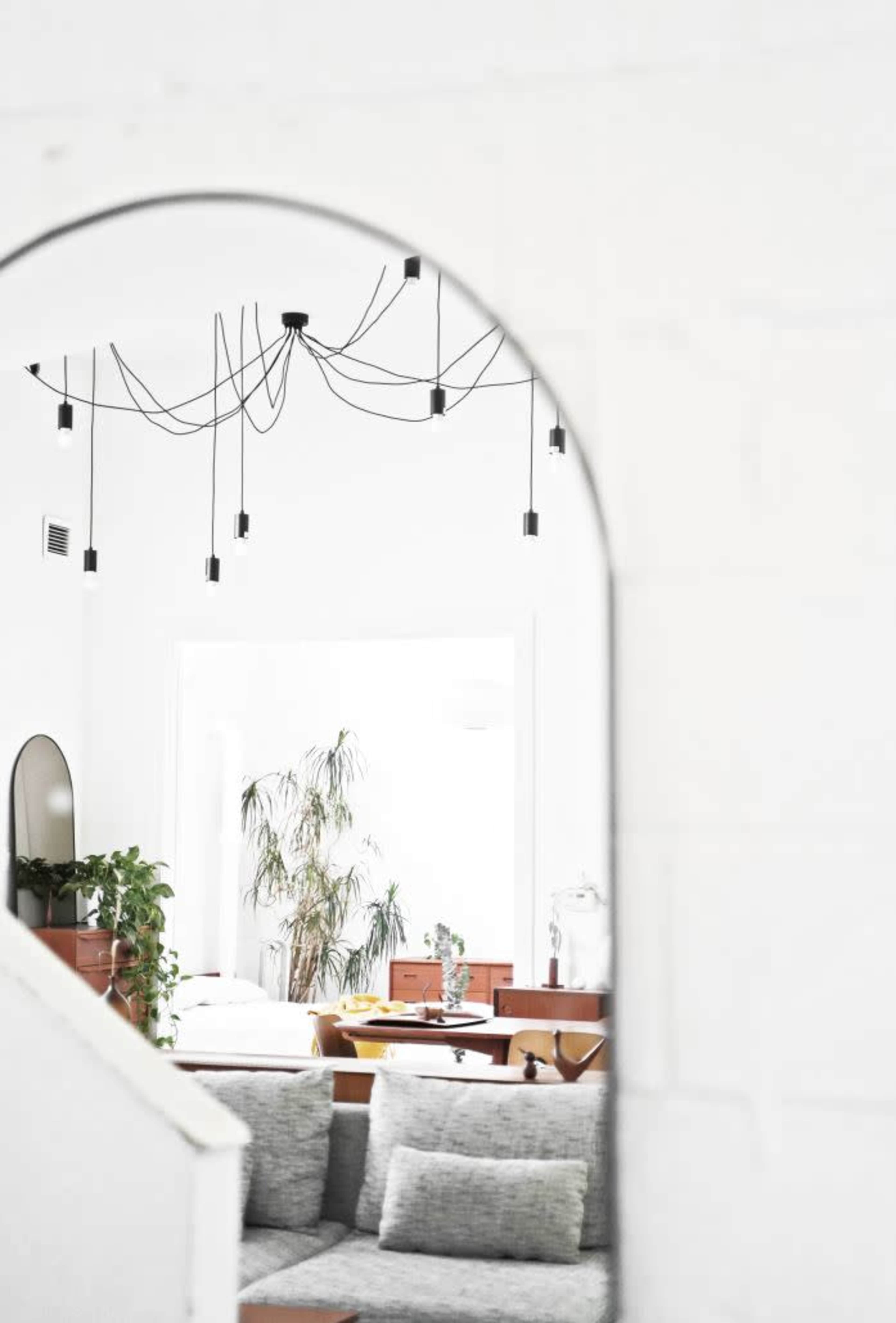 A view through an archway reveals a bright room with hanging light fixtures, plants, and minimalistic furniture.