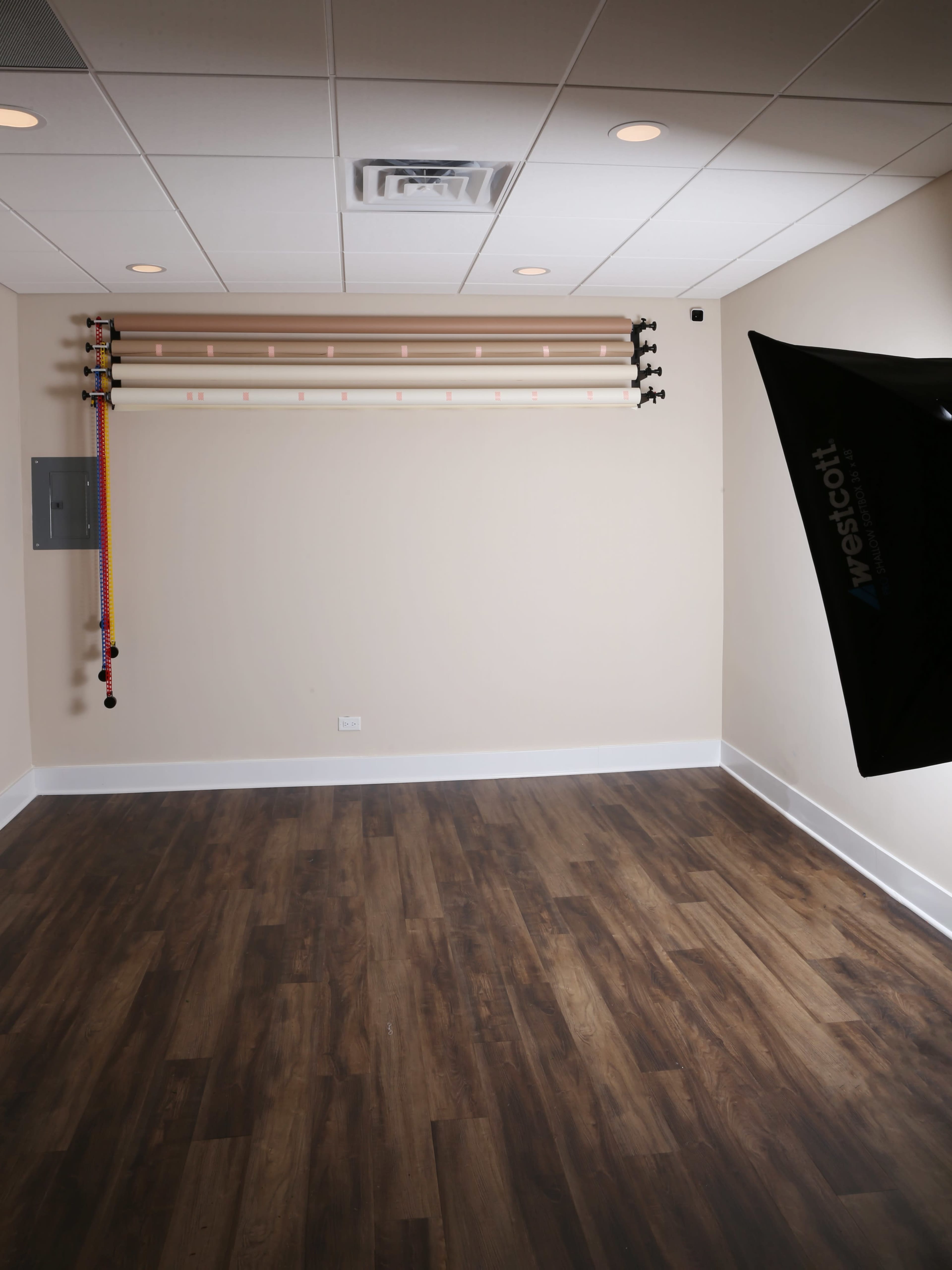 The image shows a sparsely furnished studio with wooden flooring and a wall featuring a rack of colored cables.