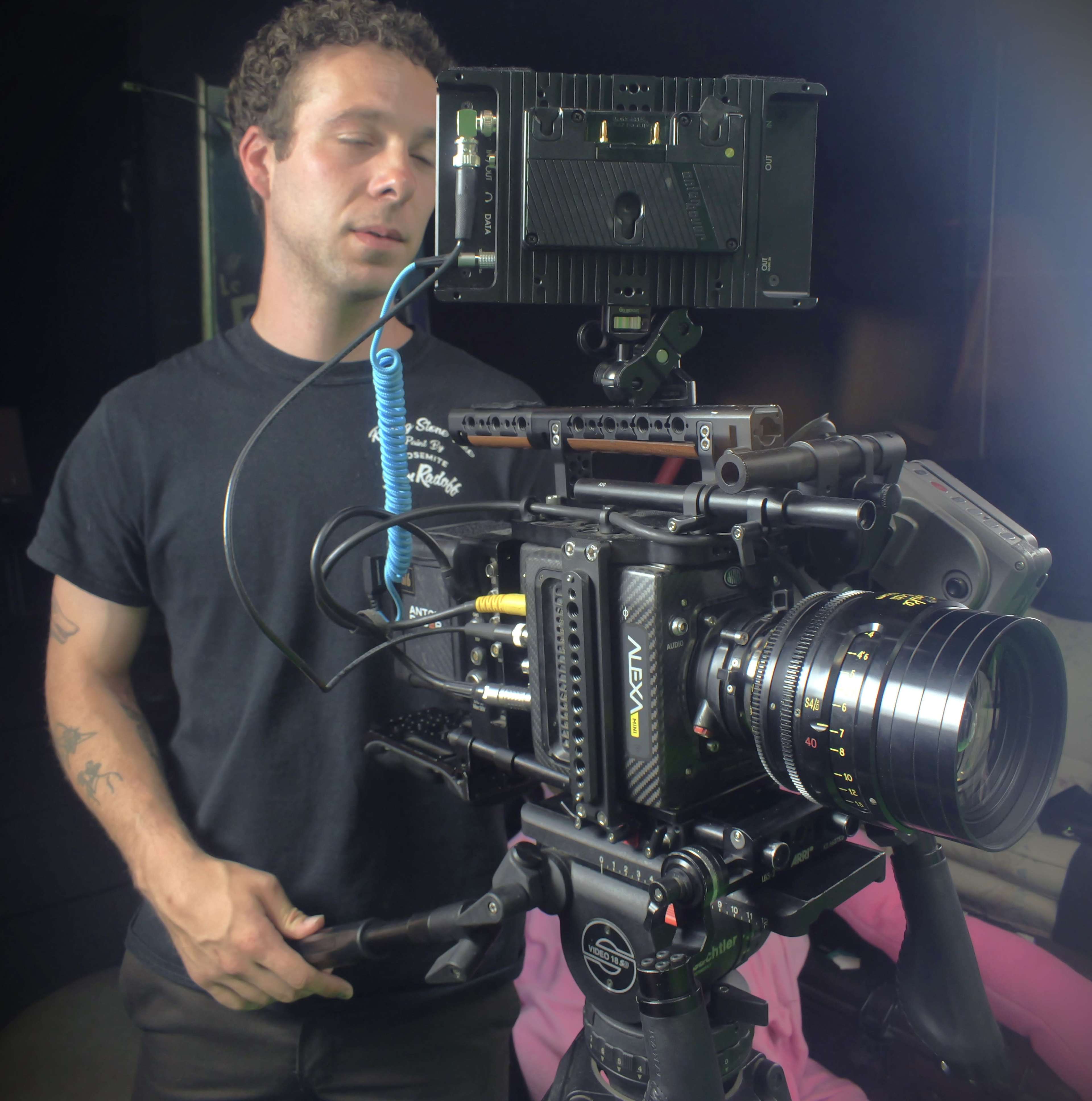 A man is setting up a professional camera rig with a large lens and external monitor in a studio environment.