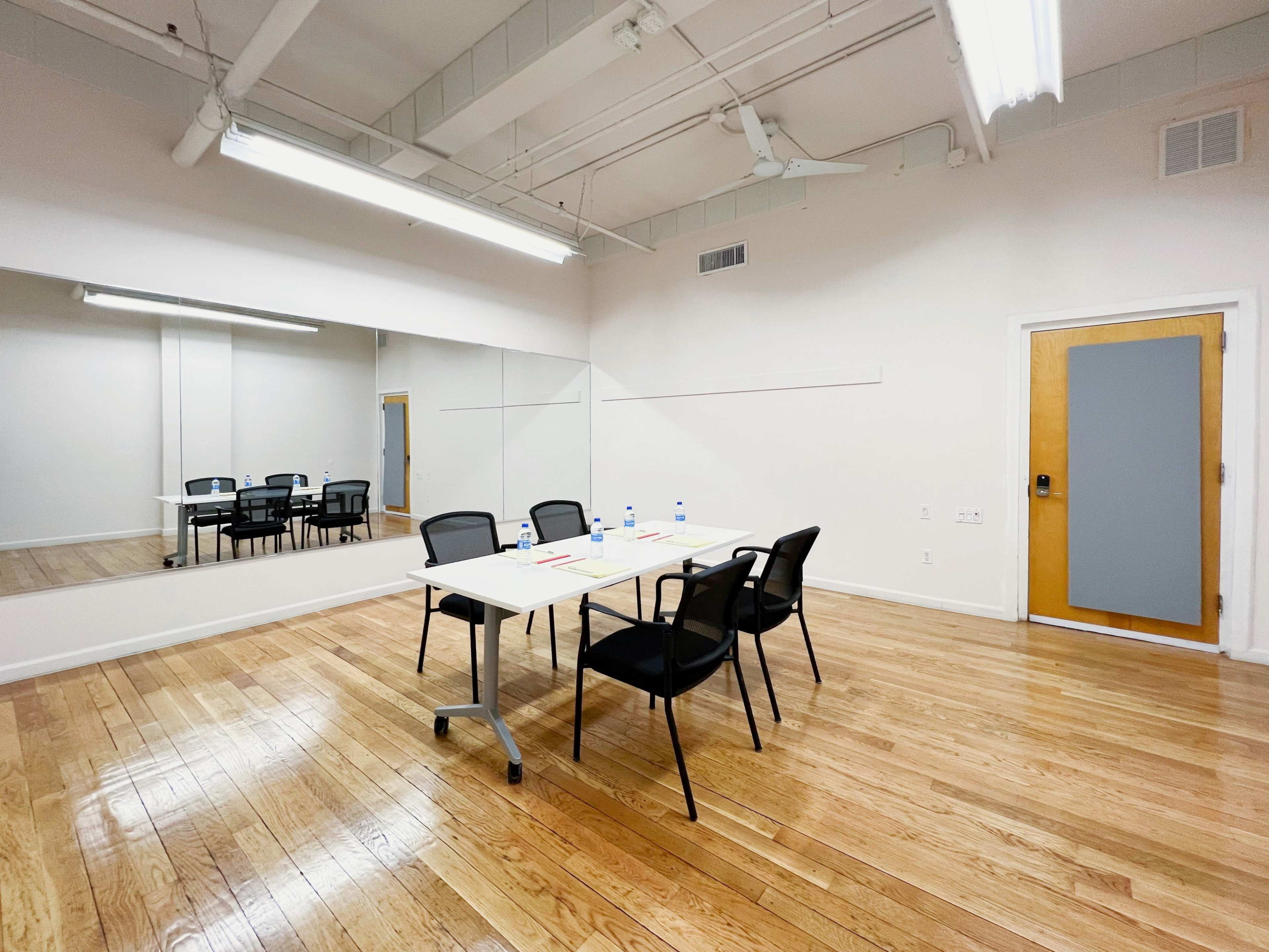 A conference room is shown with a table and chairs set up, and a large mirror on one wall.