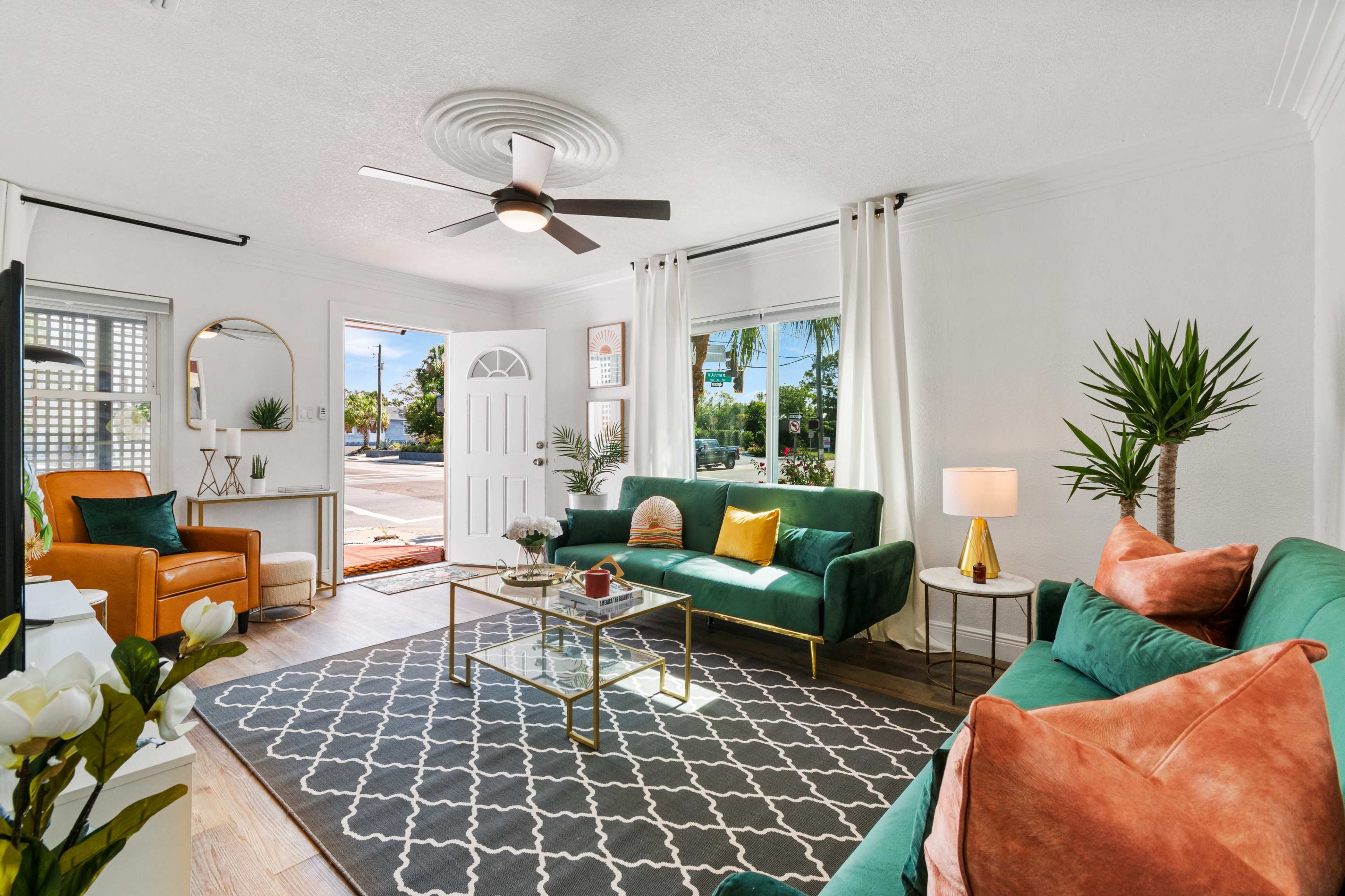A bright living room with green sofas, a coffee table, a ceiling fan, and large windows providing natural light.