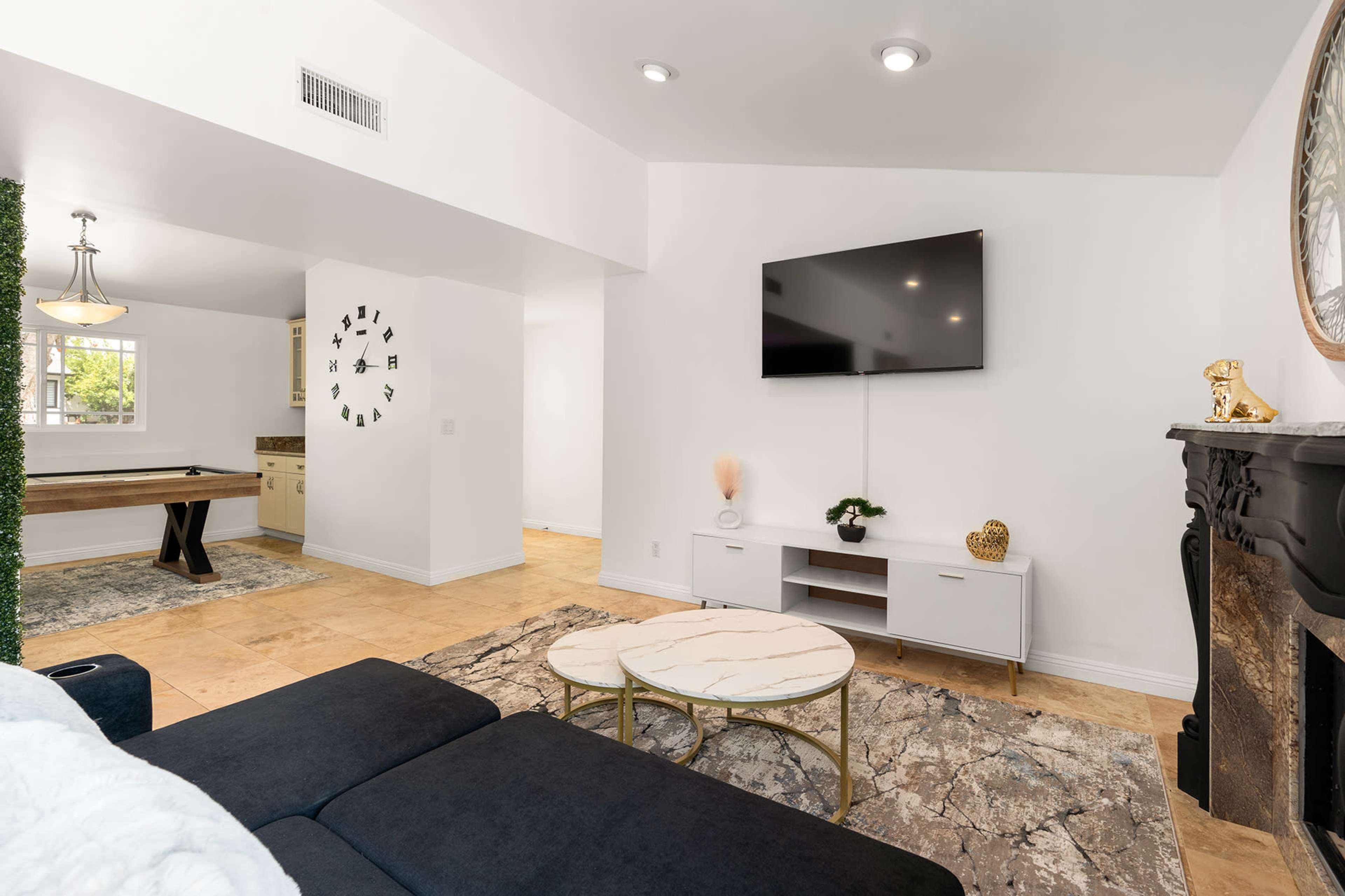 A modern living room featuring a sectional sofa, a marble coffee table, a television mounted on the wall, and a decorative fireplace.