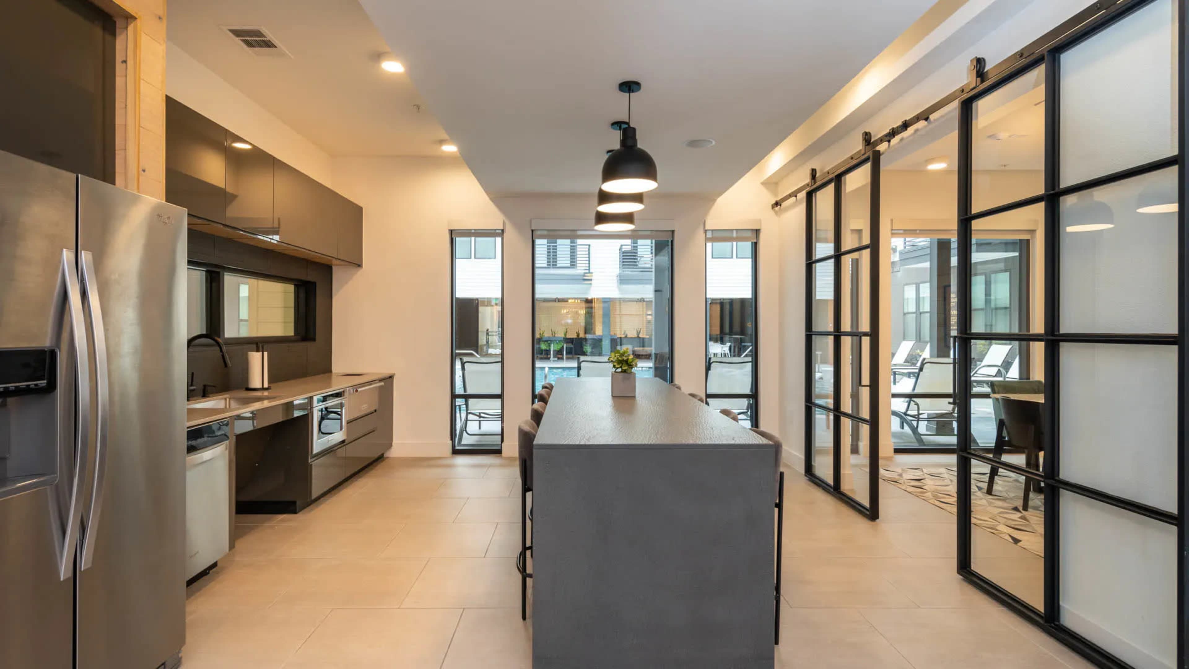 A modern kitchen with stainless steel appliances, an island with seating, and large windows leading to an outdoor patio area.