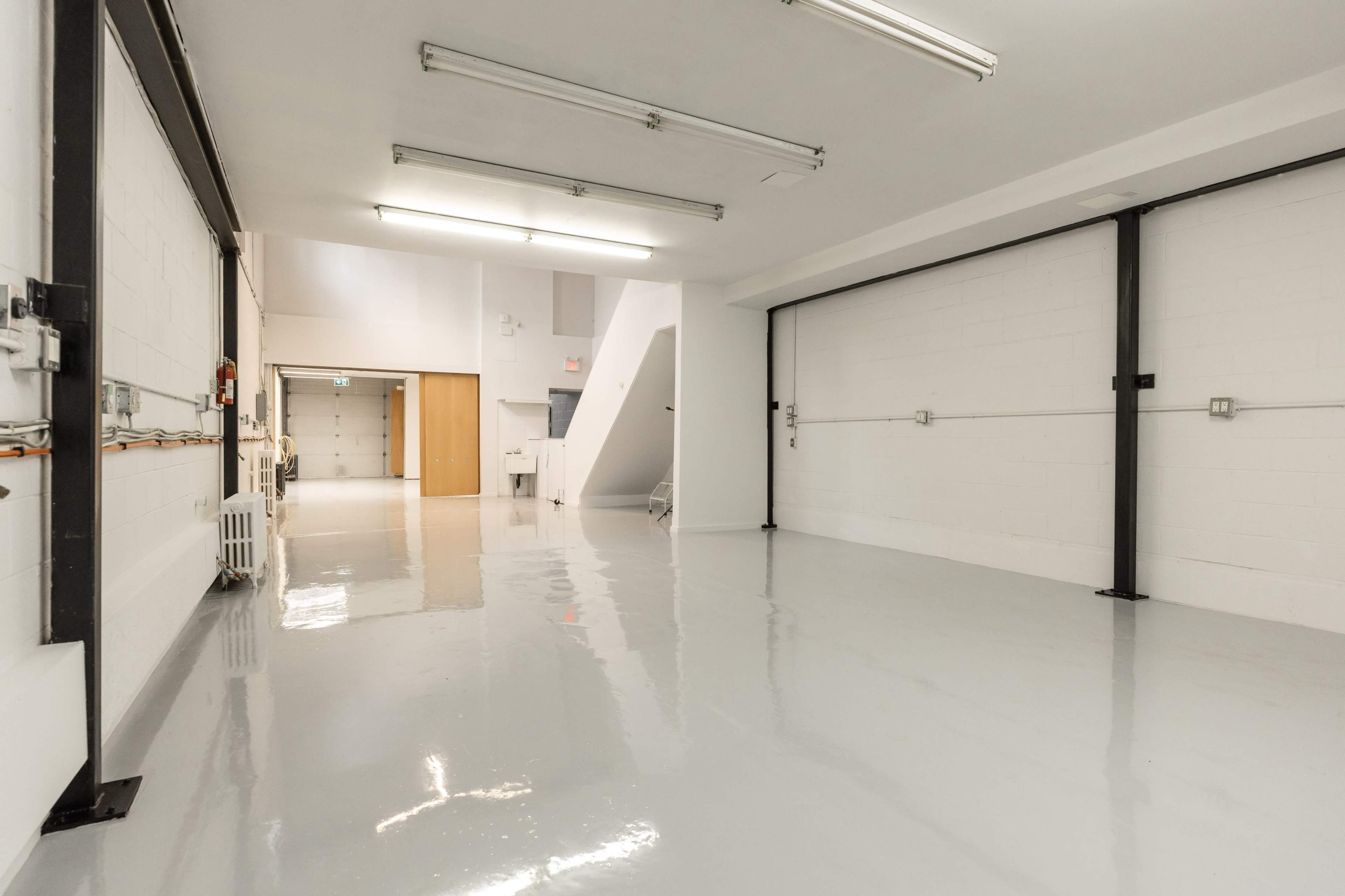 The image shows a spacious, well-lit garage or industrial room with a glossy white floor and minimal furnishings.