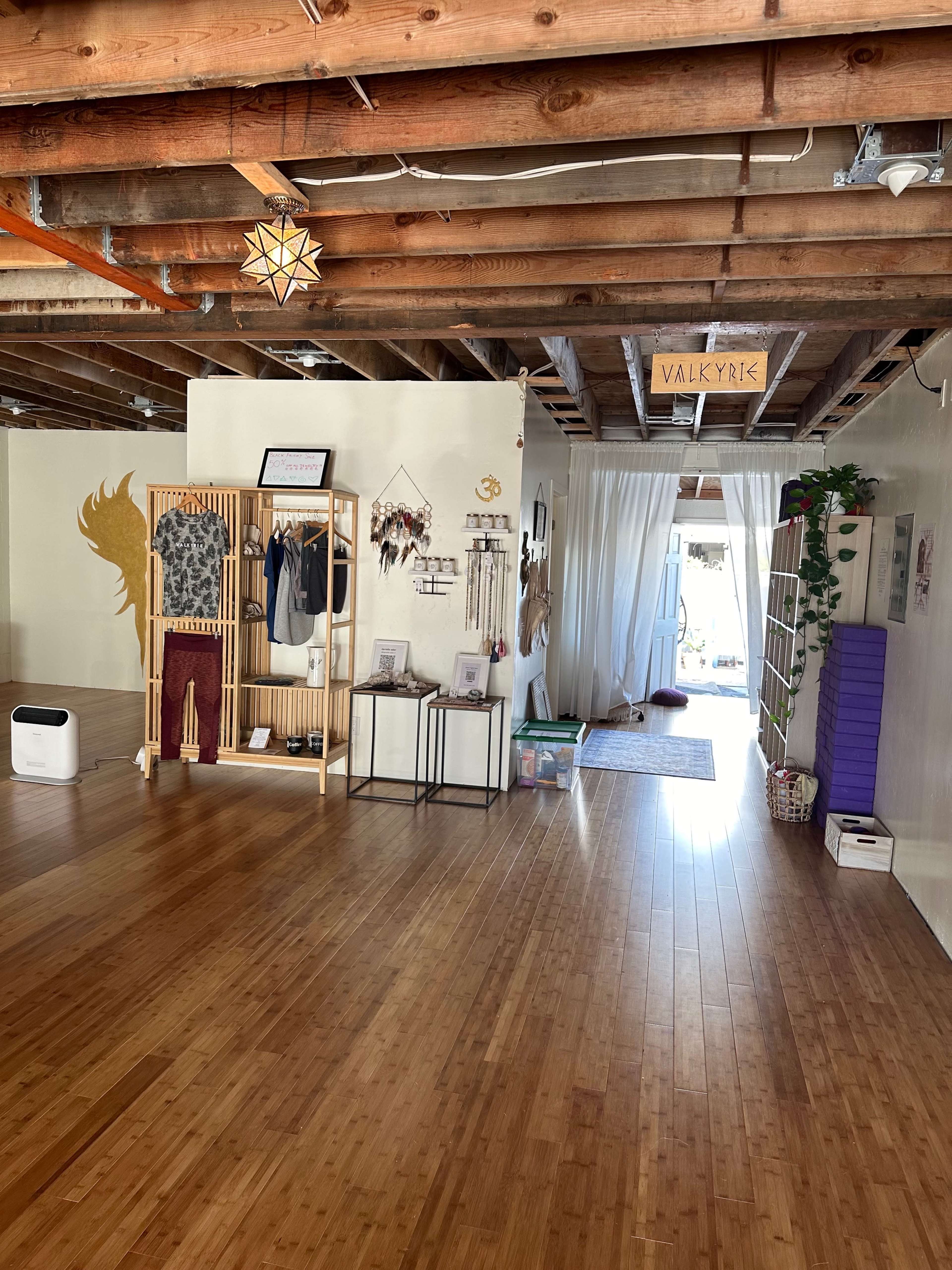 A spacious interior with wooden beams, showcasing a clean area with decorative clothing racks, various hanging items, and an open doorway leading to another space.