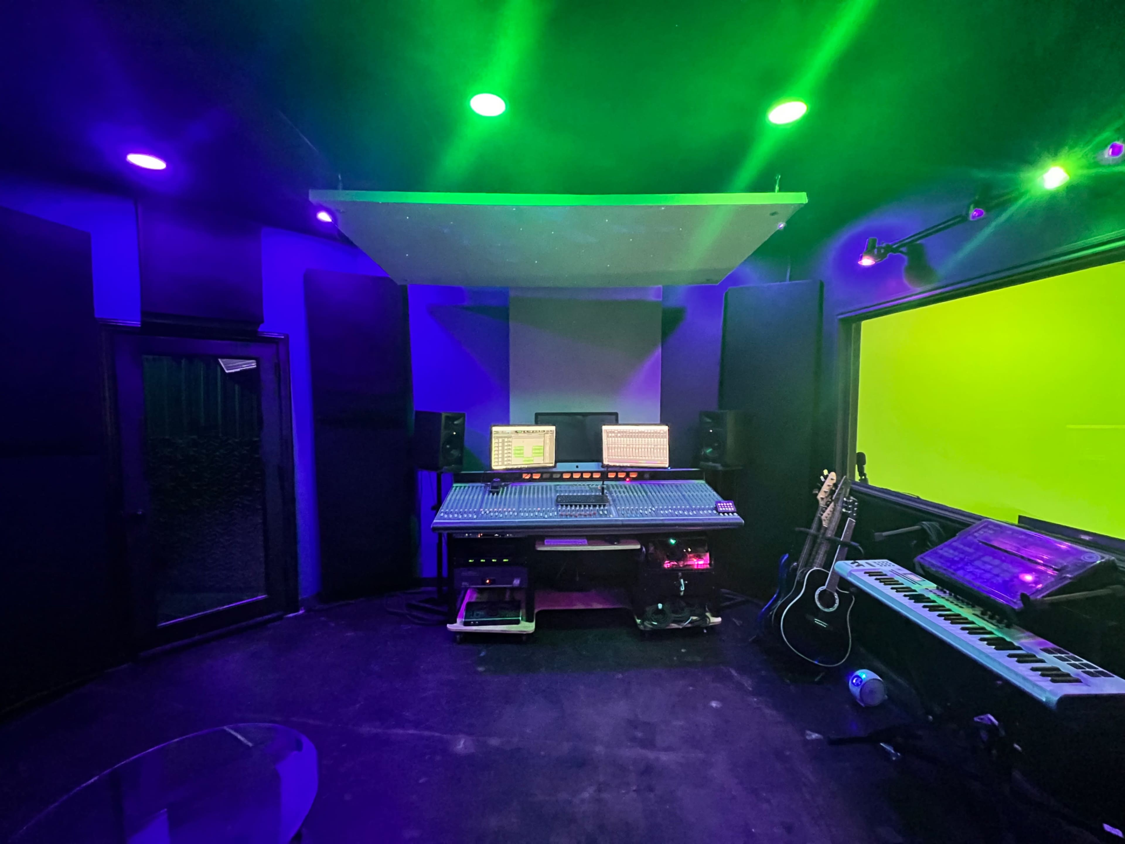 A music recording studio featuring a large mixing console, speakers, and various musical instruments, with purple and green ambient lighting.