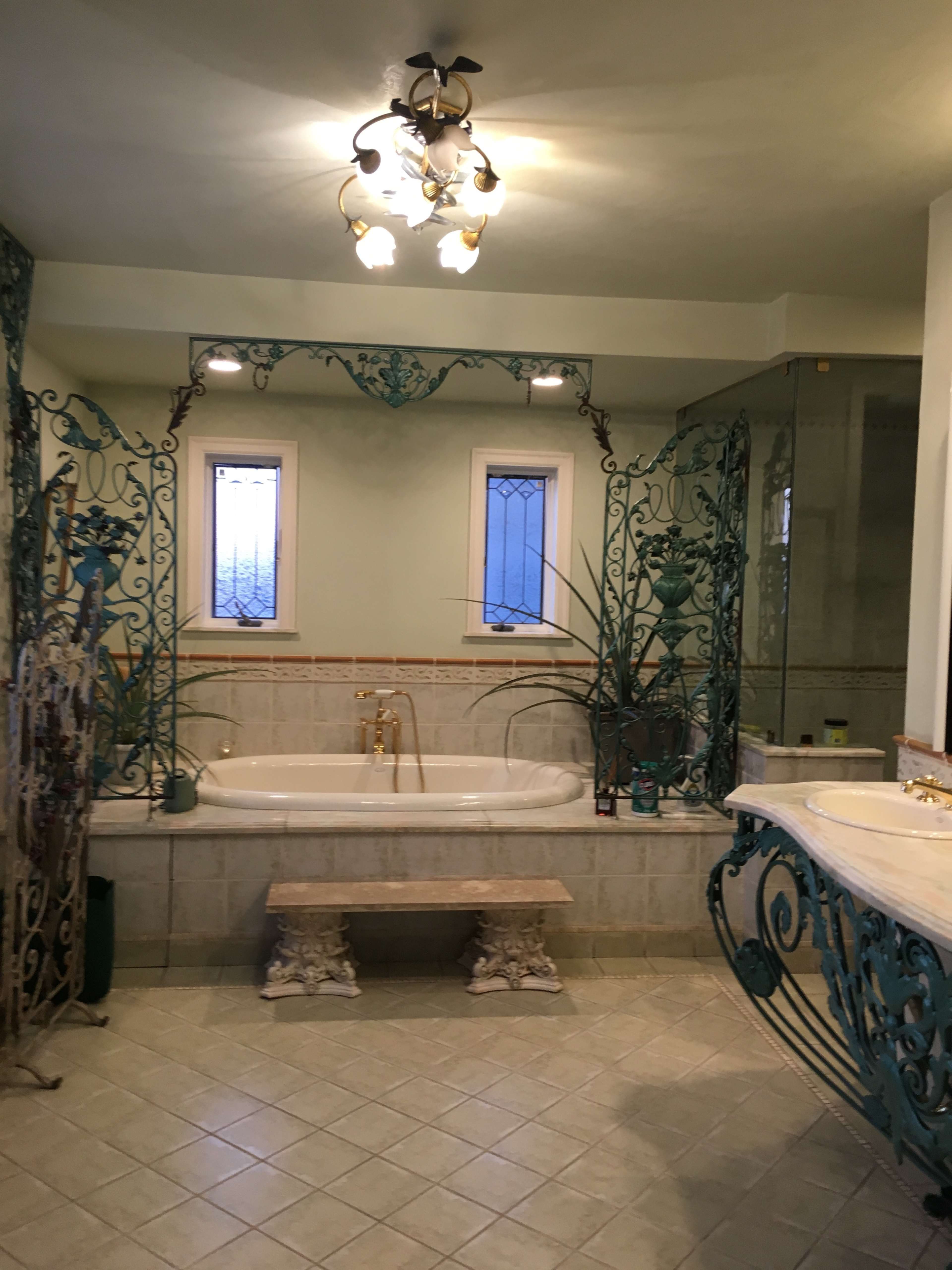 The bathroom features a large freestanding tub surrounded by decorative ironwork, a dual sink vanity, and natural light coming through two windows.
