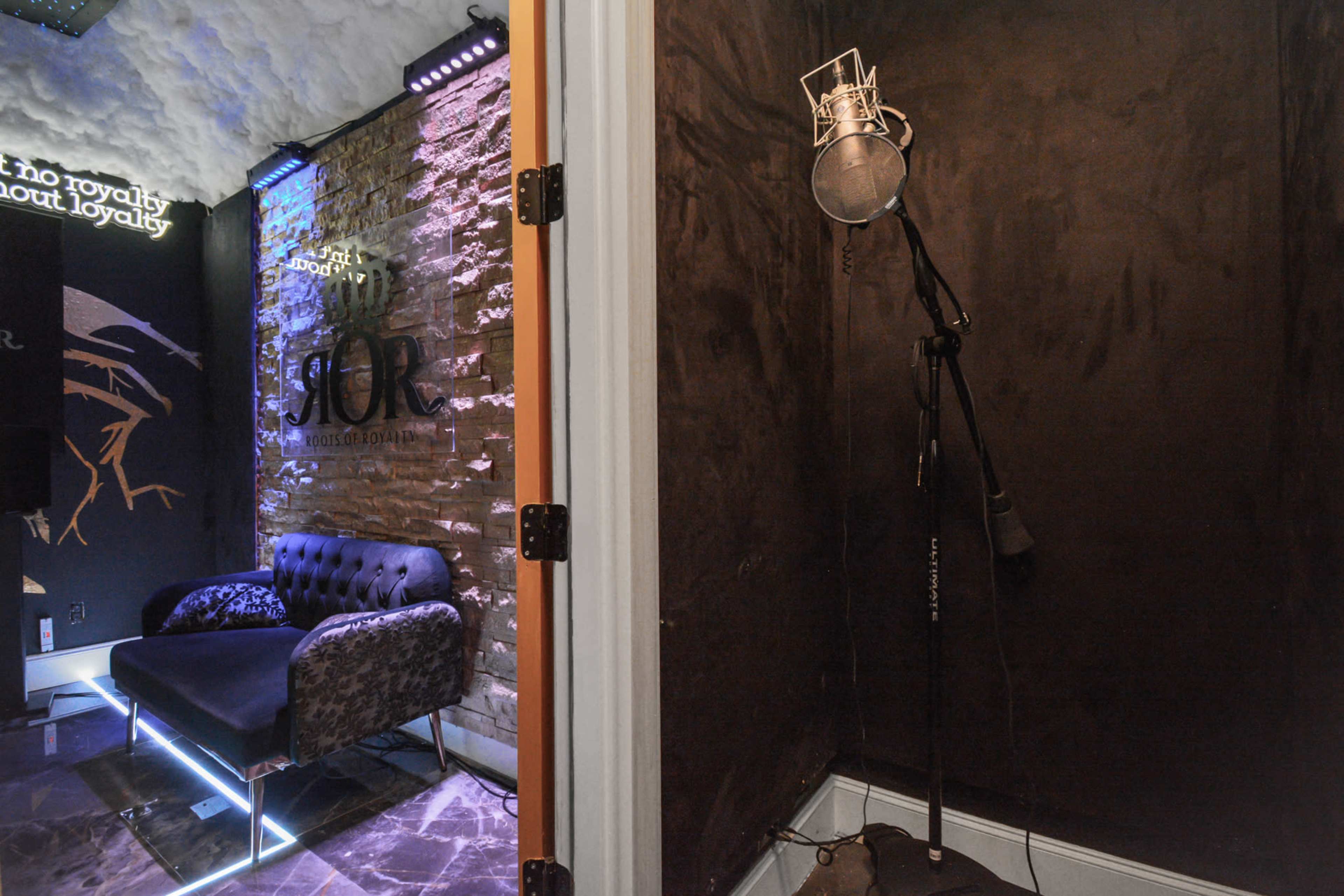 The image shows a soundproof recording booth next to a stylish lounge area with a microphone and a black couch.