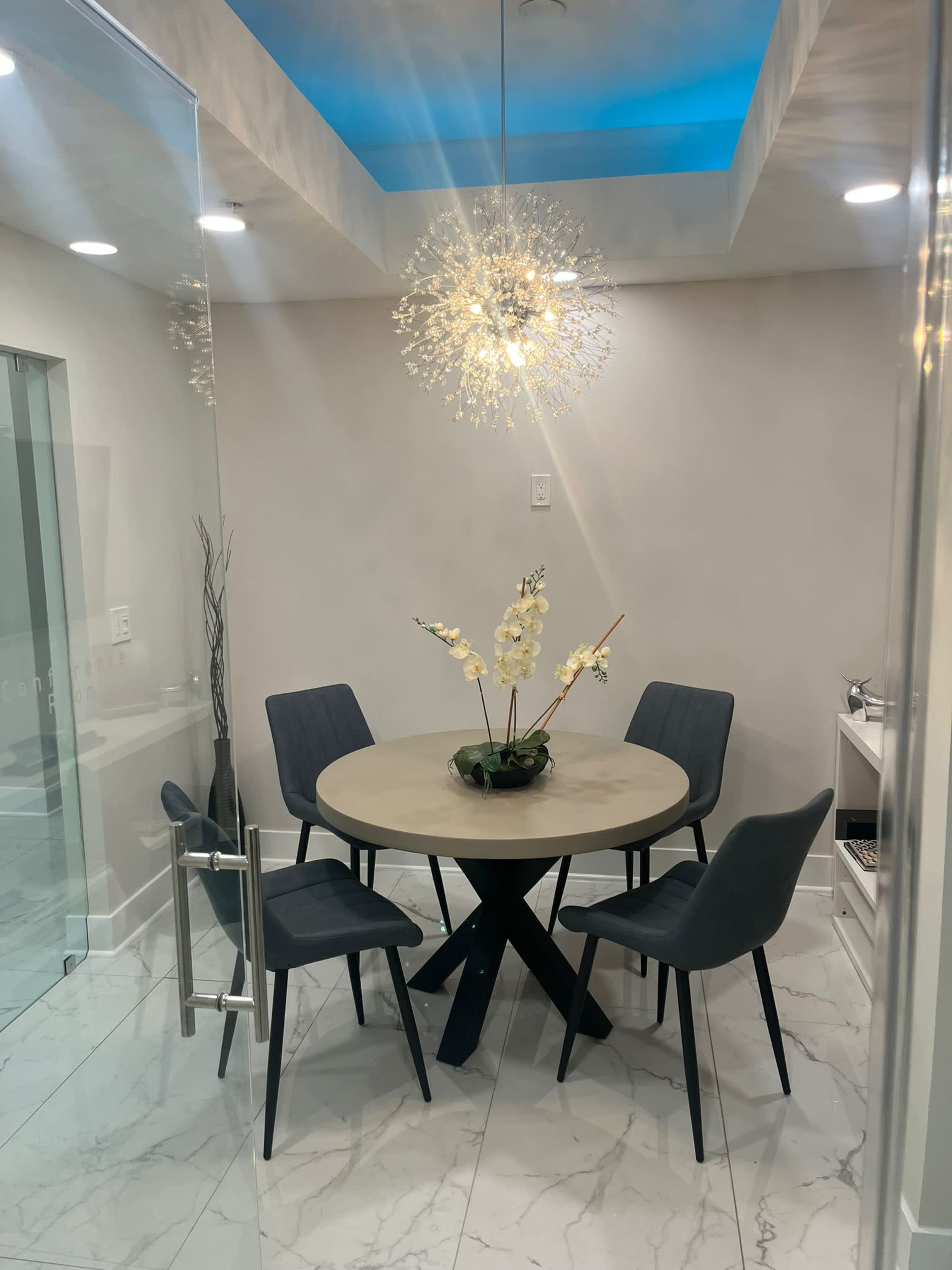 A modern dining area features a round wooden table surrounded by four upholstered chairs beneath a decorative light fixture.