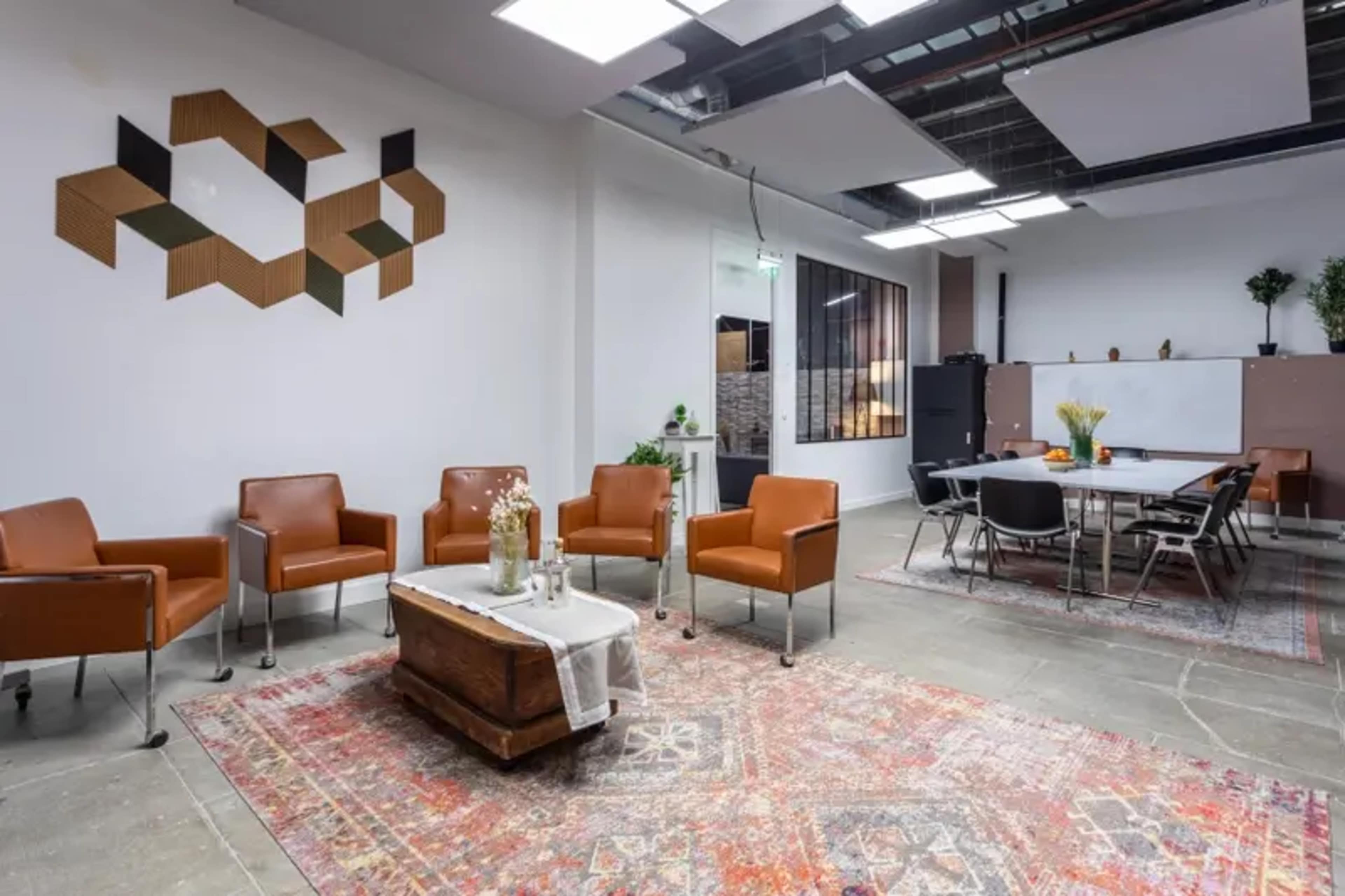 A modern meeting space with brown chairs, a wooden table, and an area rug, featuring a decorative wall with geometric designs.