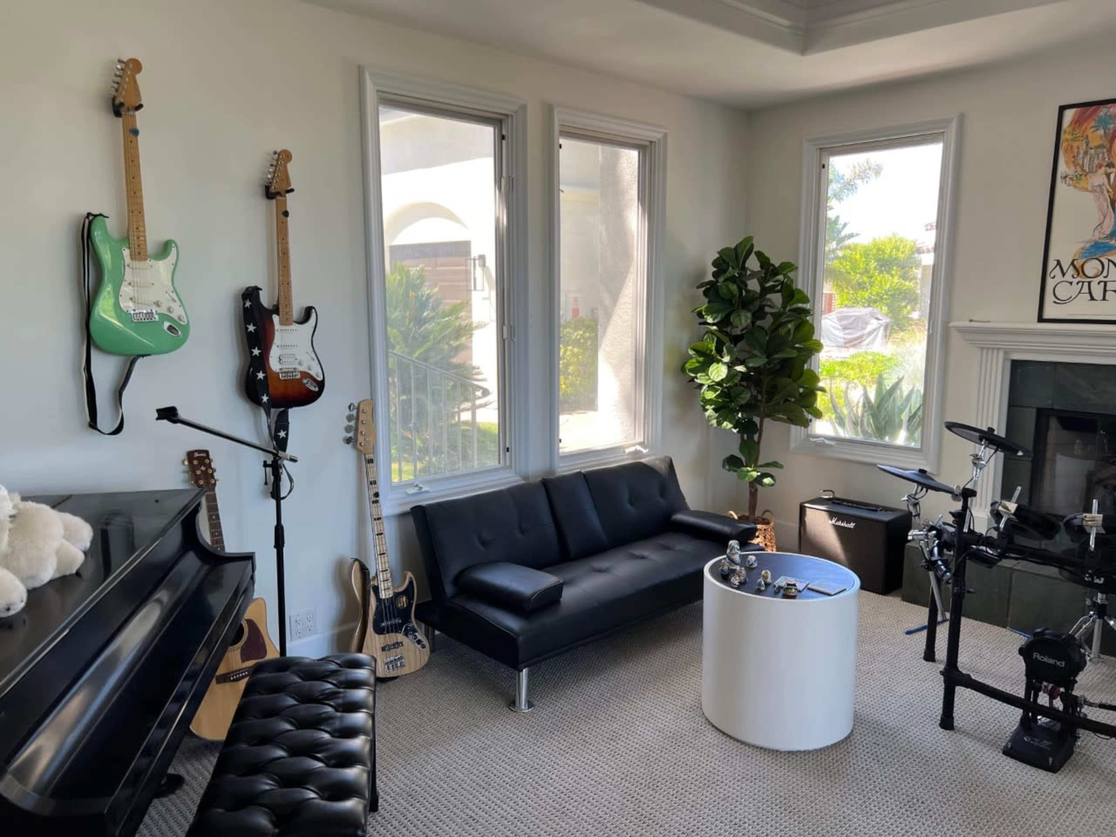 The scene features a modern living room with a black sofa, a piano, multiple electric guitars on the wall, an electronic drum set, and large windows that provide natural light.