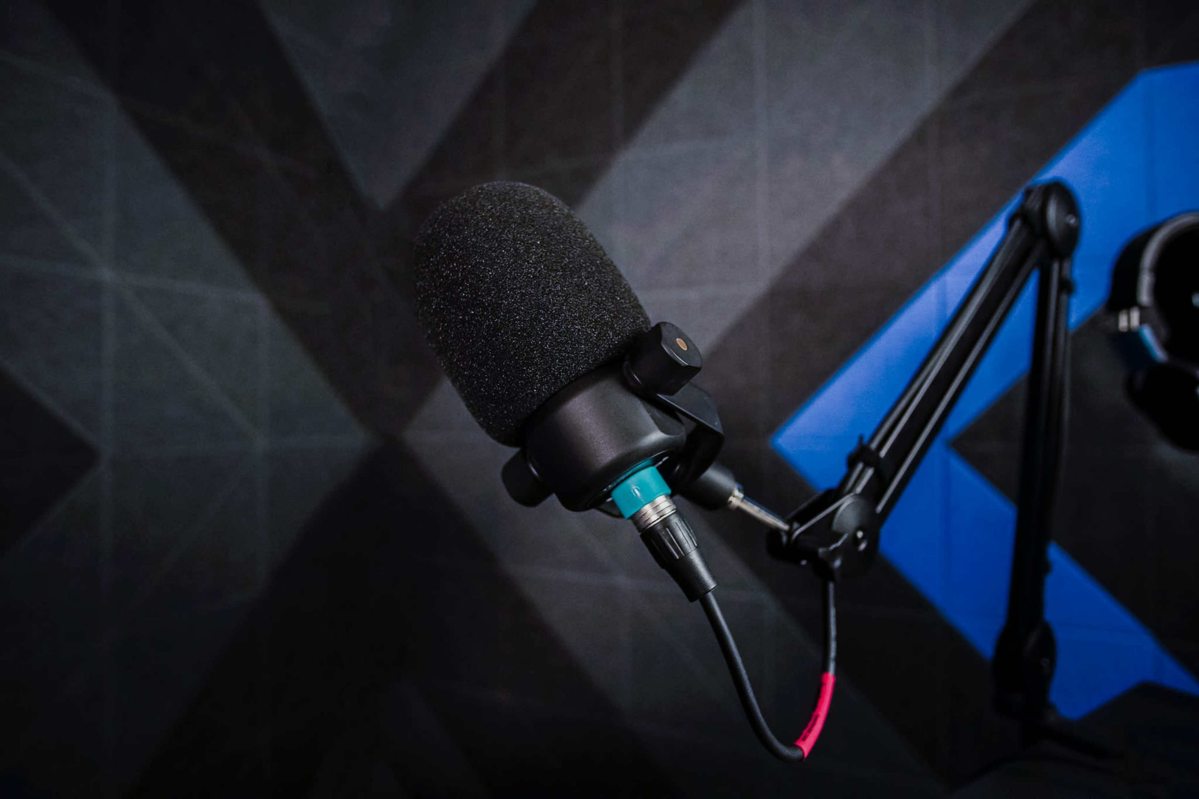 A black microphone is mounted on an adjustable arm against a geometric background.