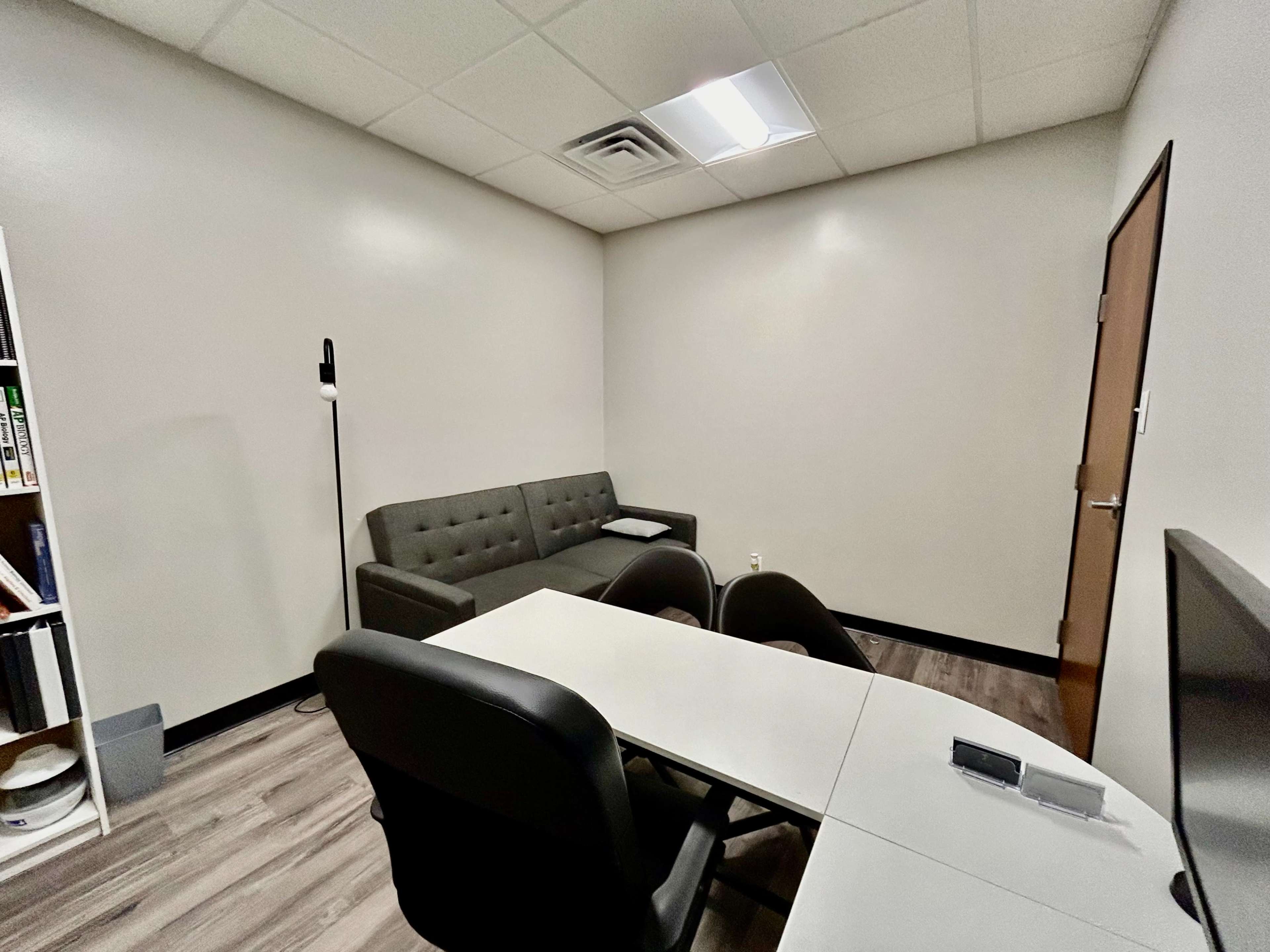 A small office or meeting room featuring a grey couch, a table with chairs, and a door.