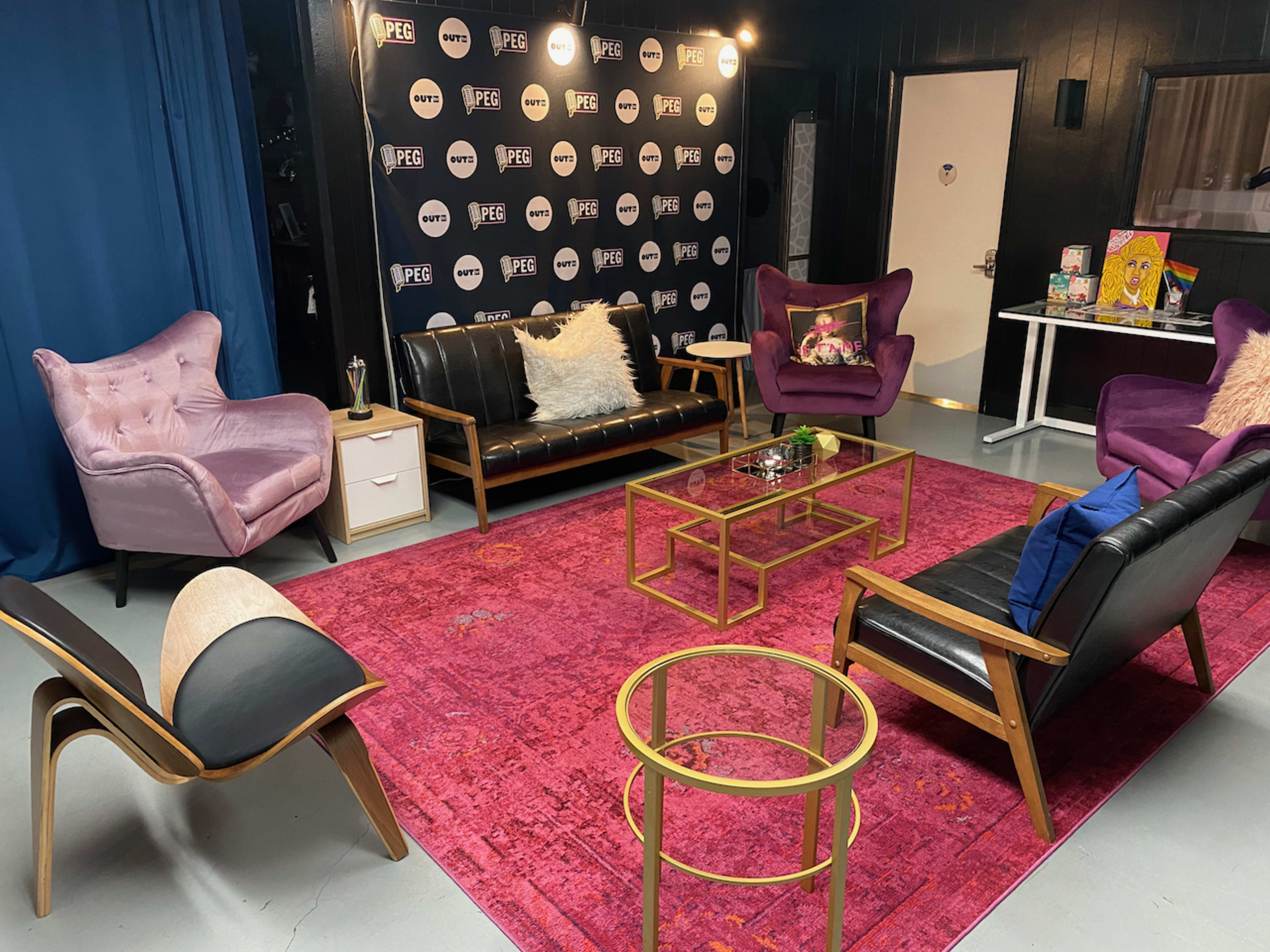 The image shows a modern lounge area with a pink area rug, several stylish chairs, a glass coffee table, and a wall featuring black and white branding.