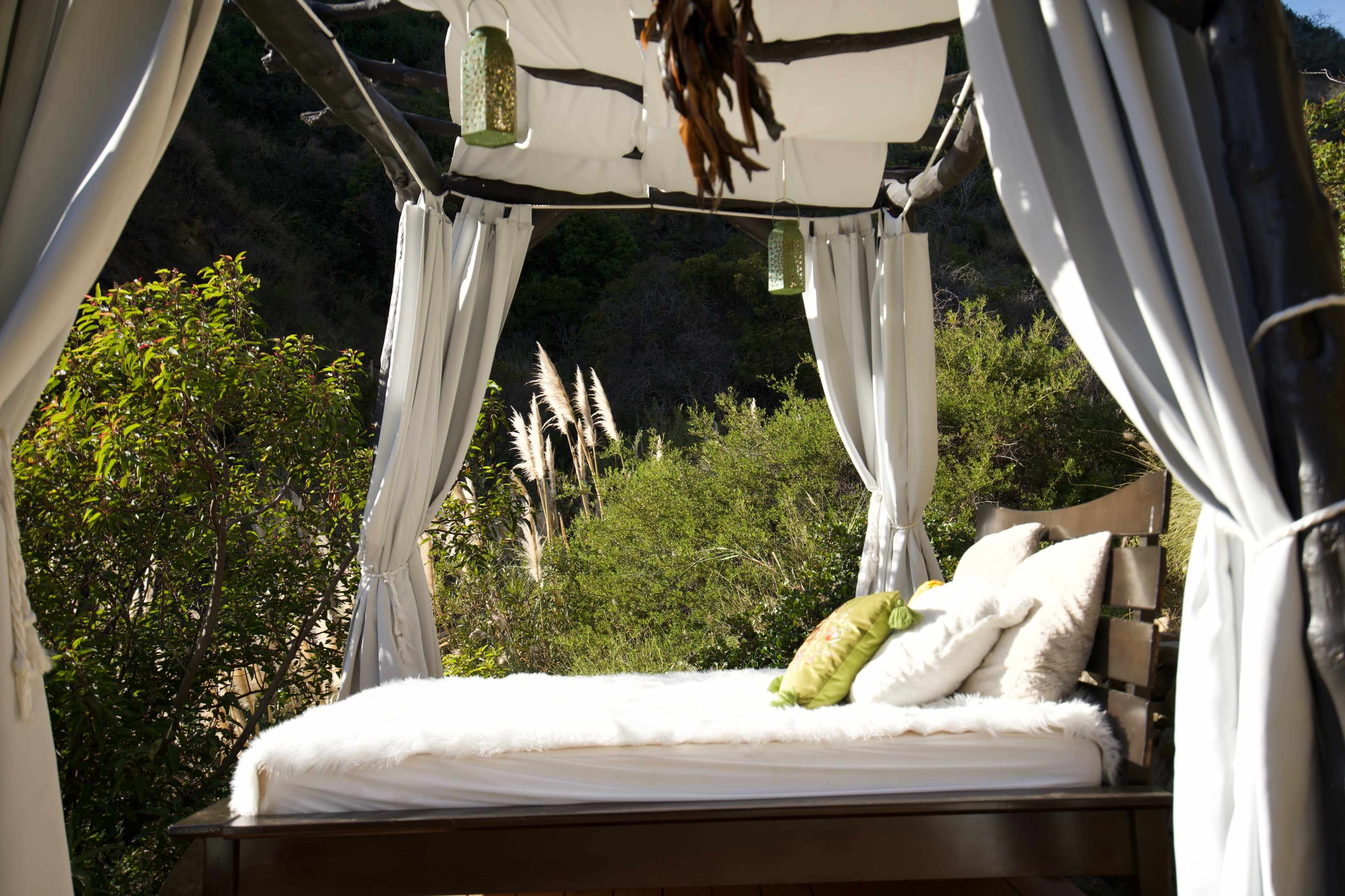 A cozy outdoor daybed is surrounded by lush greenery and soft curtains.