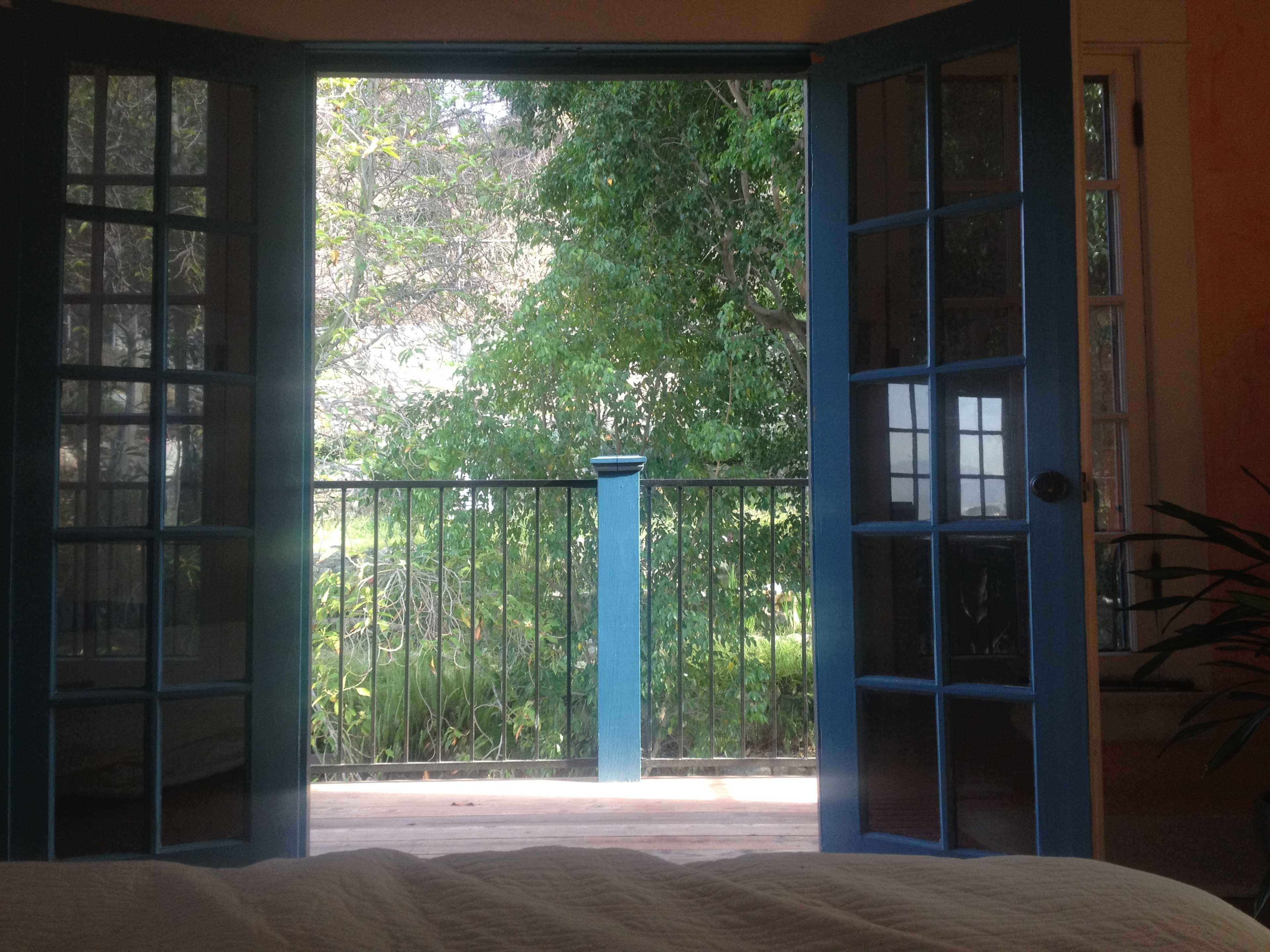 A pair of blue French doors opens to a balcony overlooking a lush green garden.