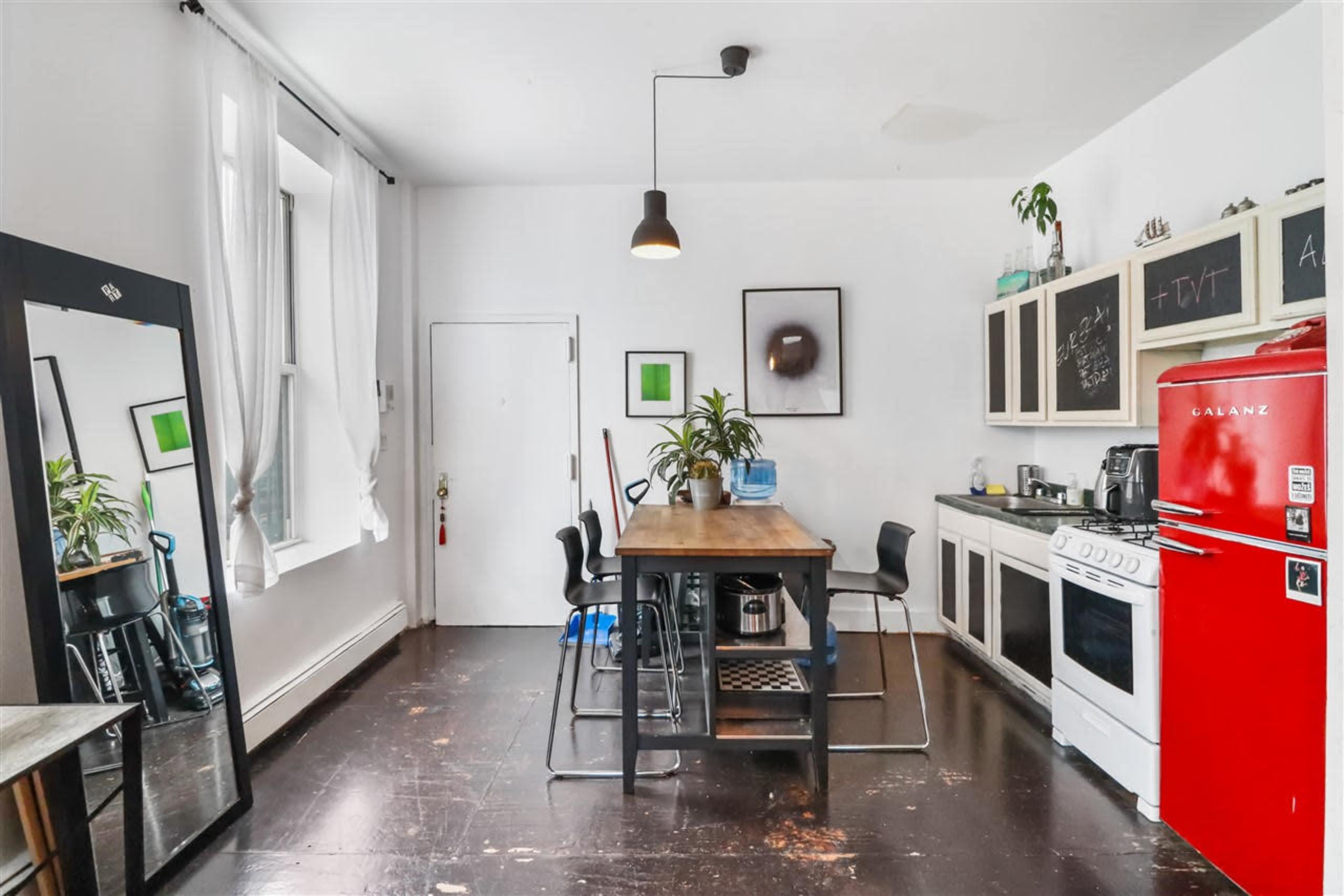 The image shows a modern kitchen area featuring a wooden table with chairs, a red refrigerator, and black cabinetry.