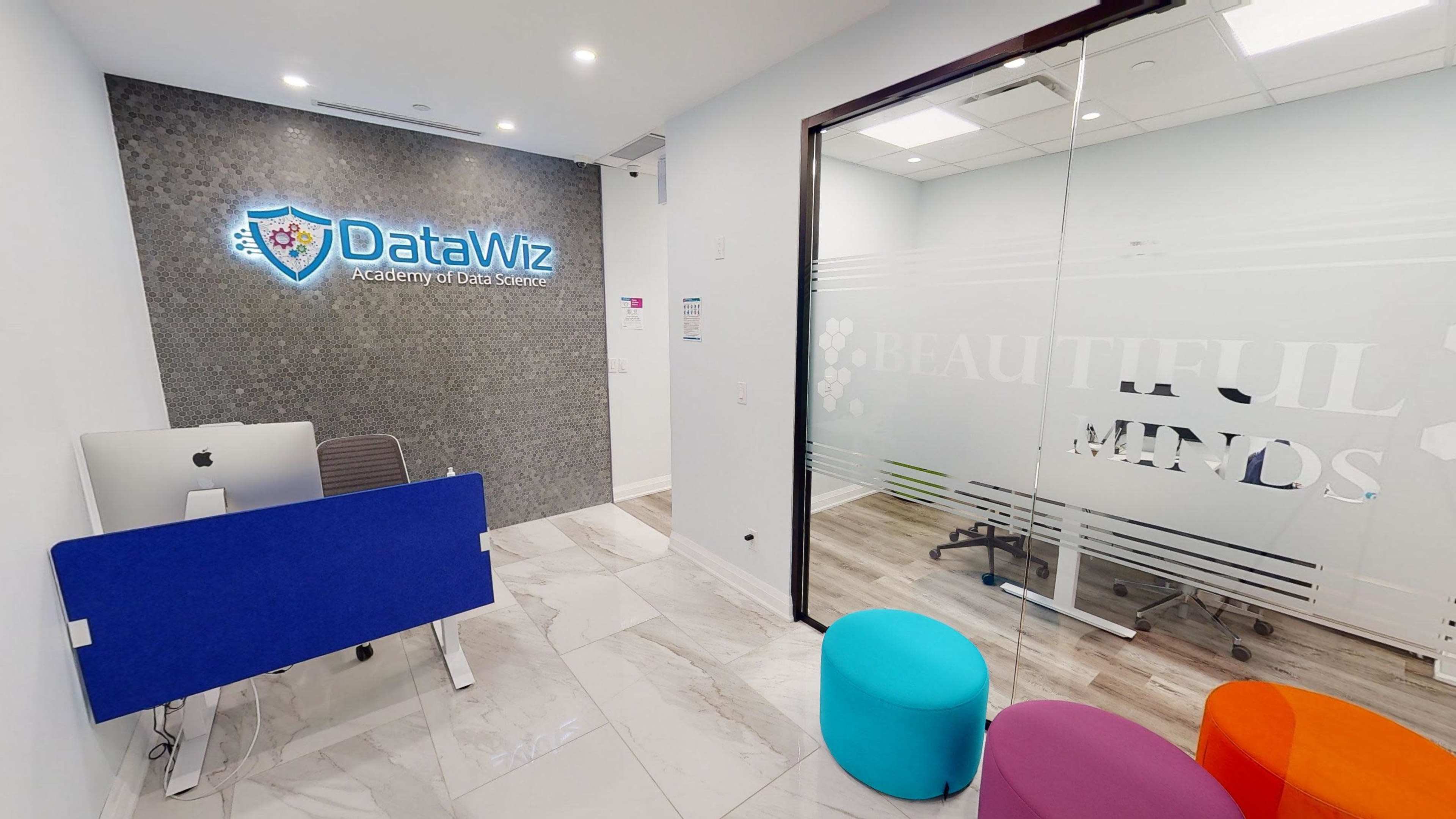 A modern office reception area with the "DataWiz Academy of Data Science" logo on the wall and colorful seating options visible in the foreground.