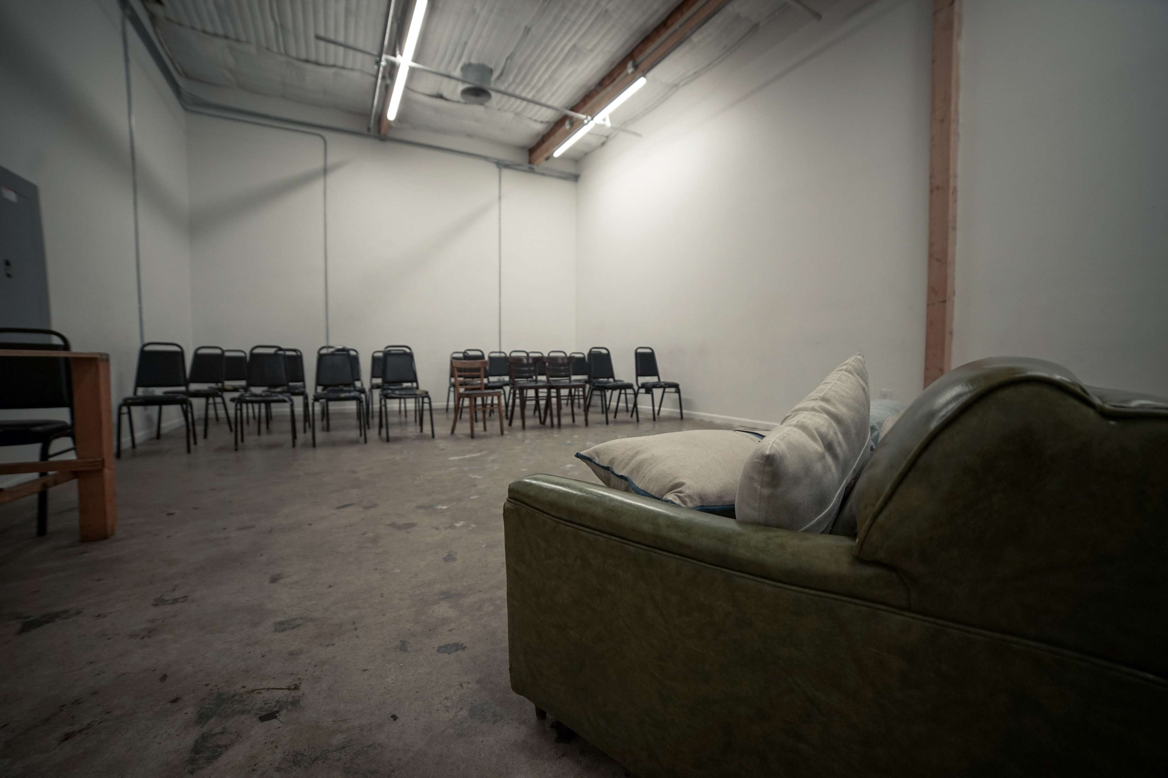 A sparse room features a green couch and a set of chairs arranged in rows facing a small table against the far wall.