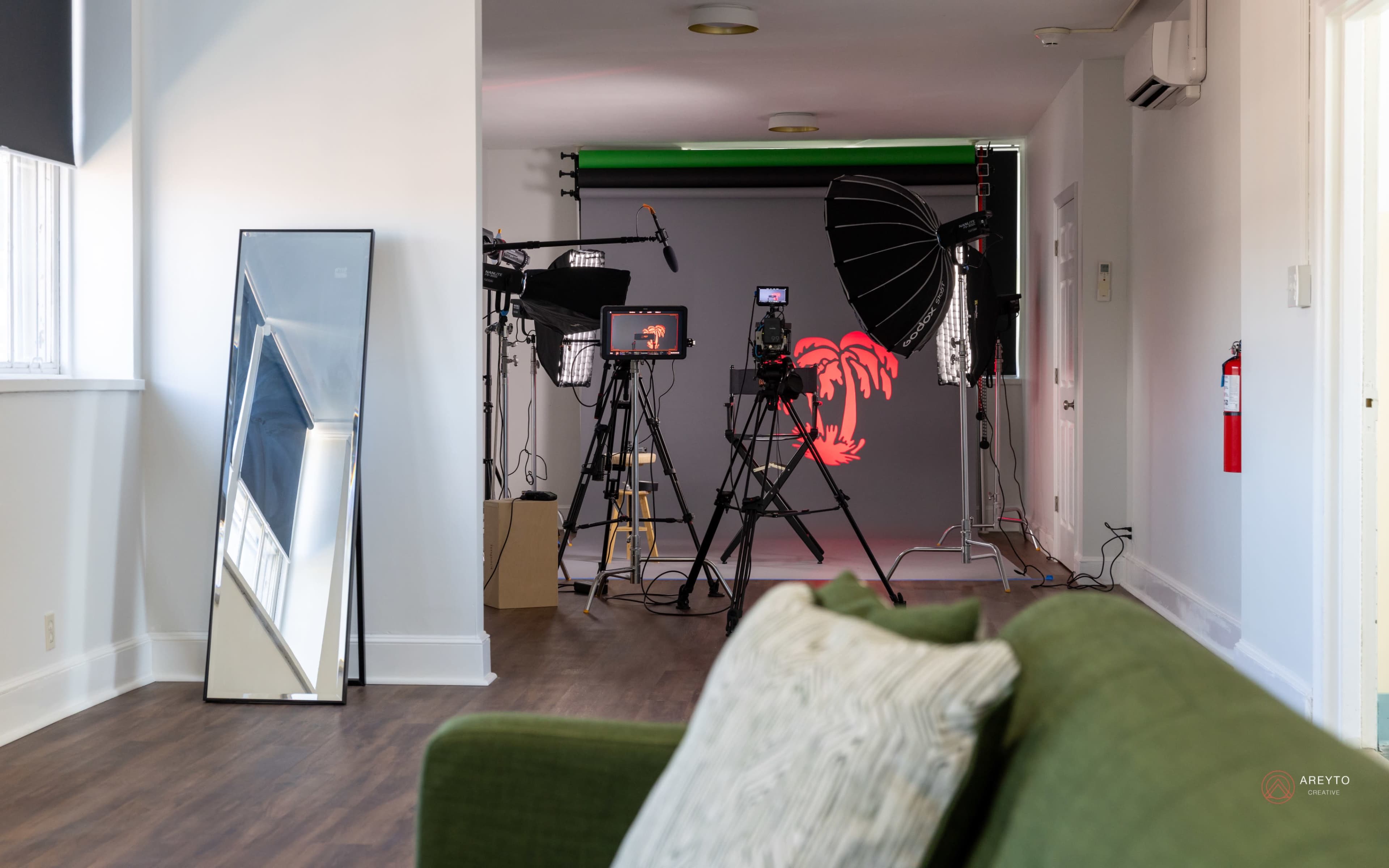 The image shows a well-lit production area featuring cameras and lighting equipment set up in front of a backdrop, with a green screen partially visible.