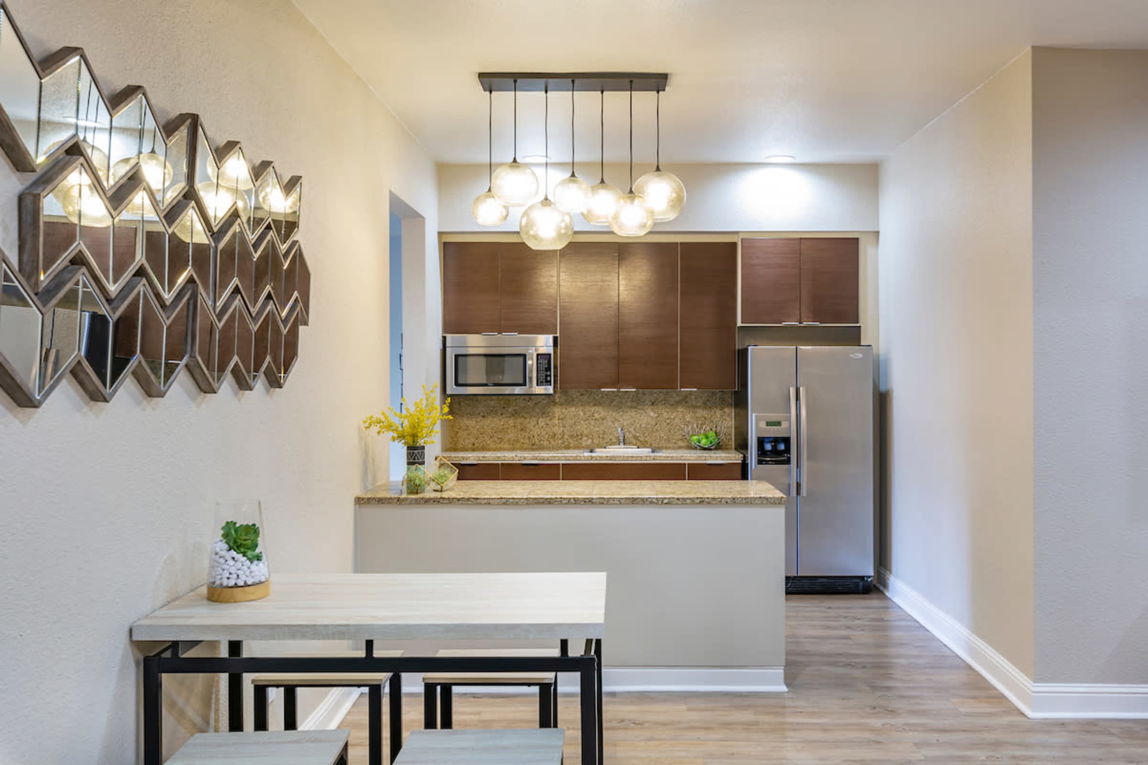 A modern kitchen features wooden cabinets, stainless steel appliances, and a dining table with benches.