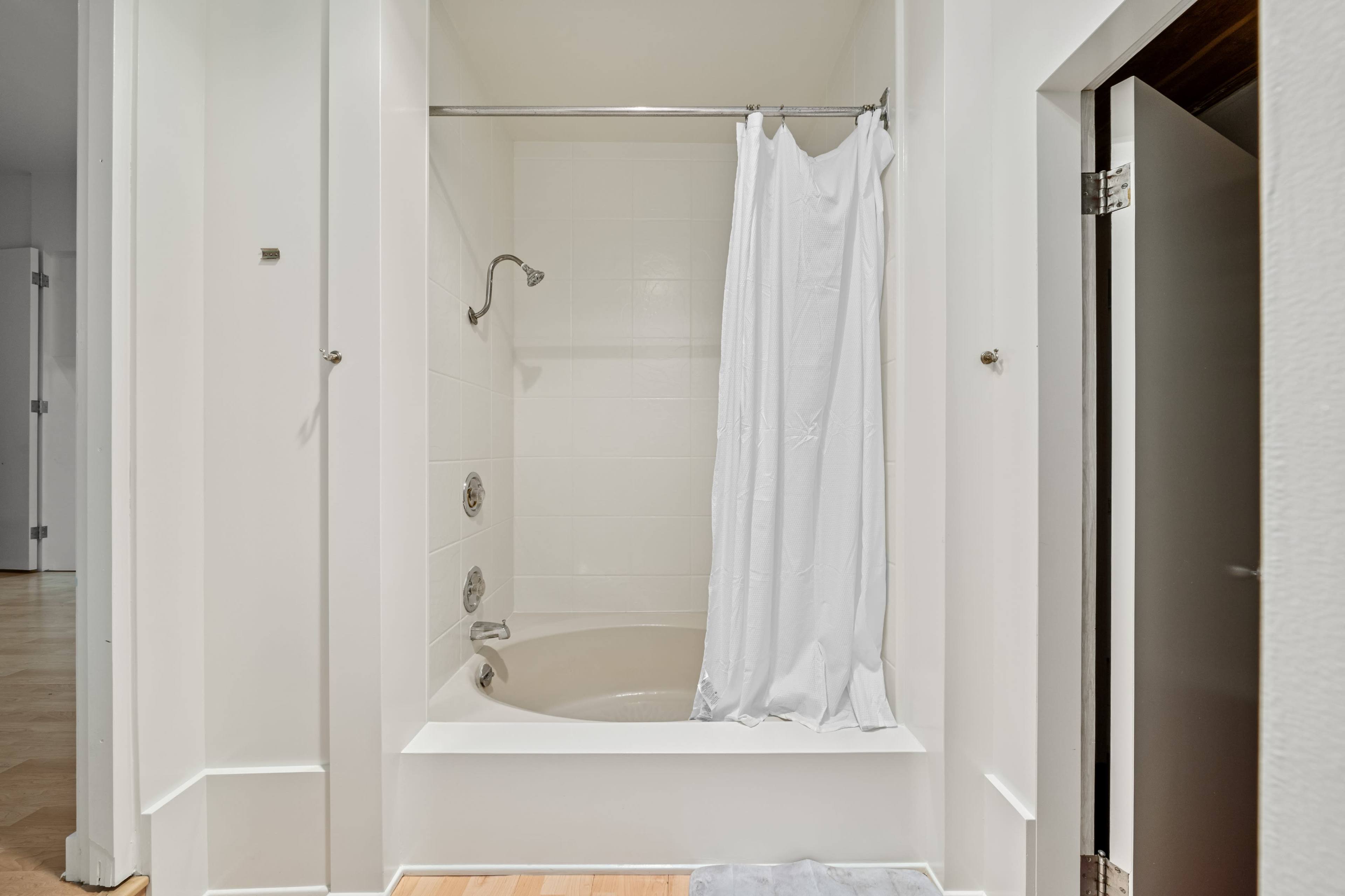 A white-tiled bathroom featuring a bathtub with a shower curtain and a showerhead.