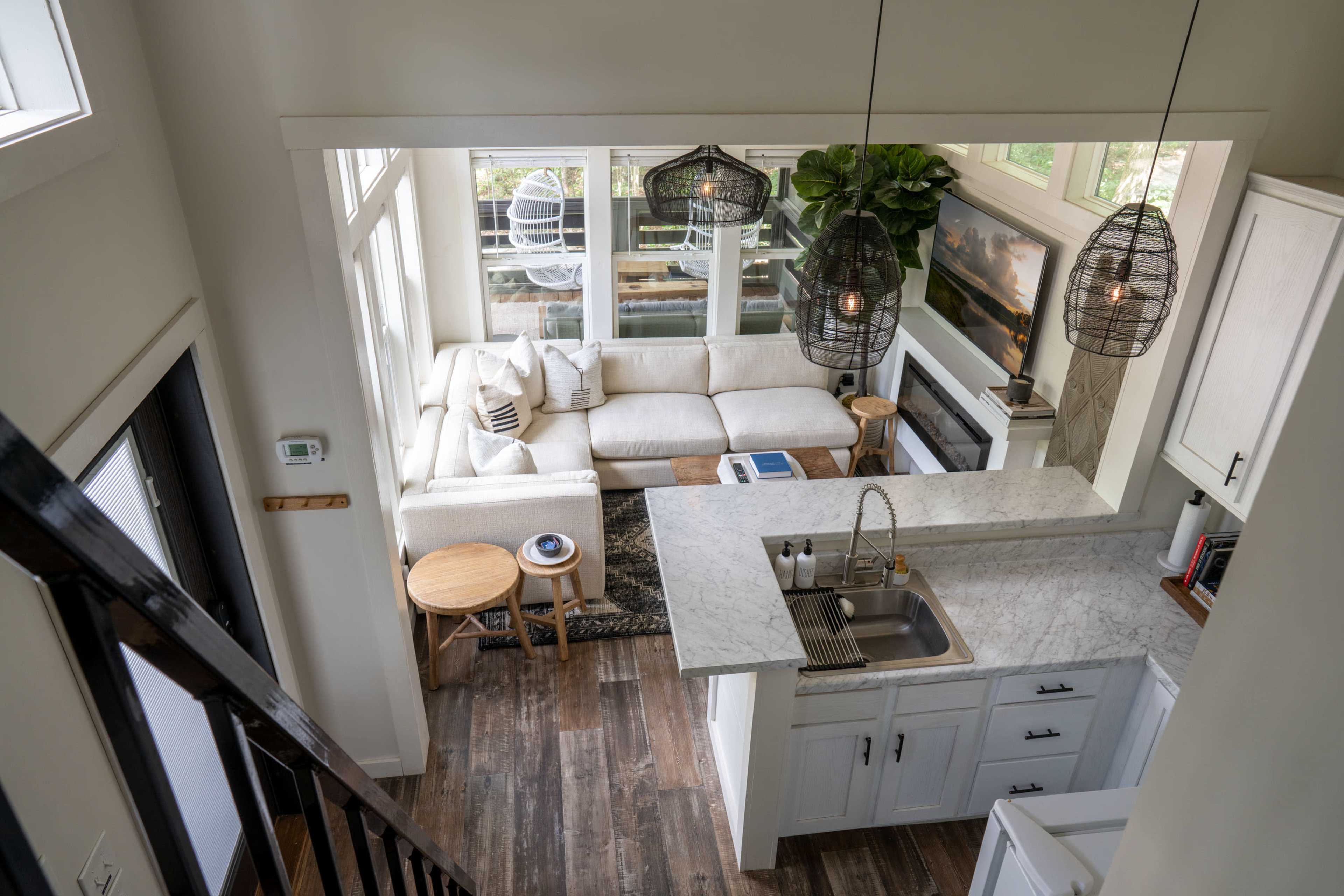 An open-plan living space and kitchen with a white sectional sofa, a wooden table, and pendant lighting.