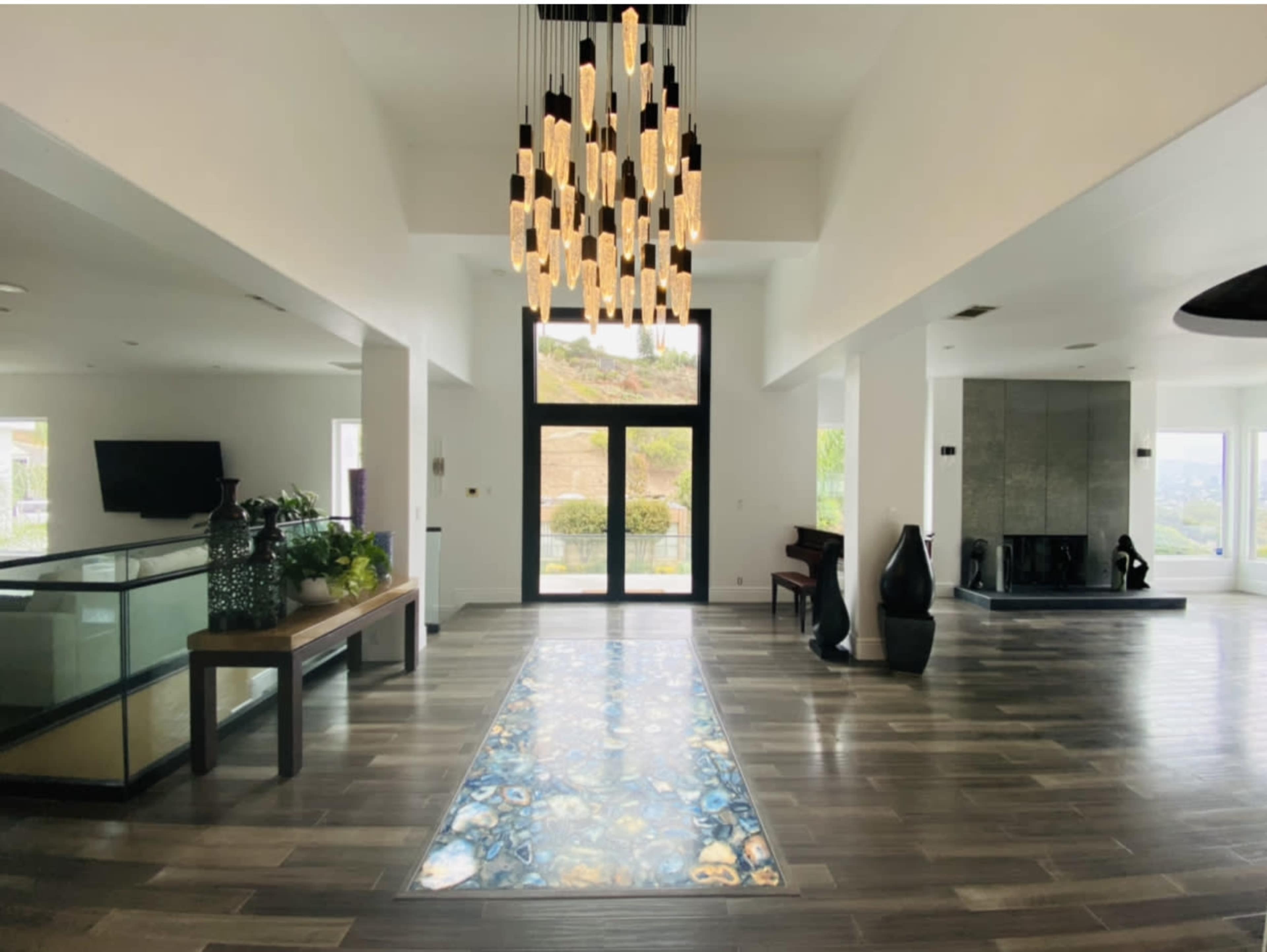 The image shows a spacious, modern interior with a unique illuminated pathway, tall ceiling, and large windows that overlook a scenic view.