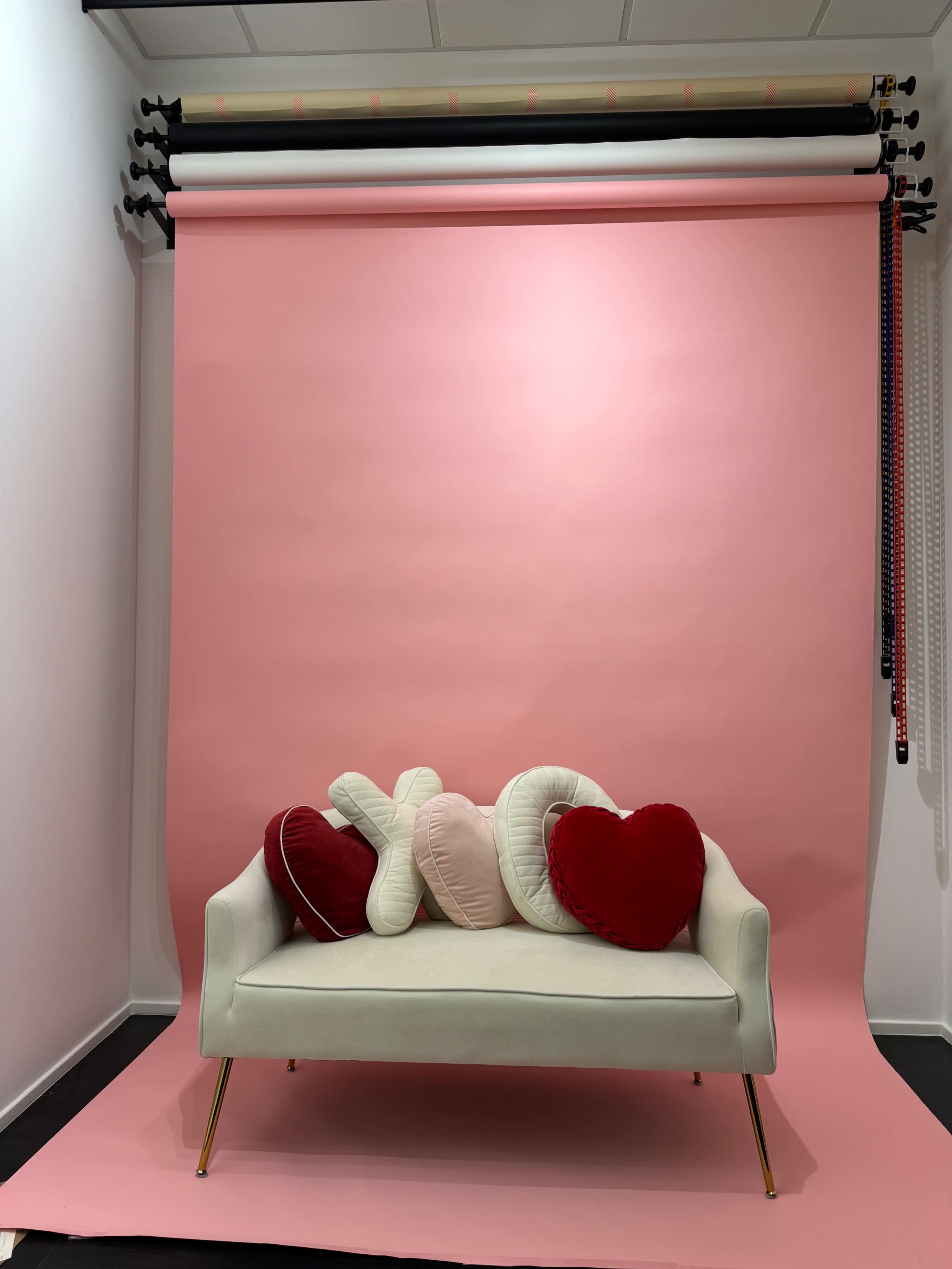 A white sofa with plush heart-shaped cushions is positioned against a pink backdrop.
