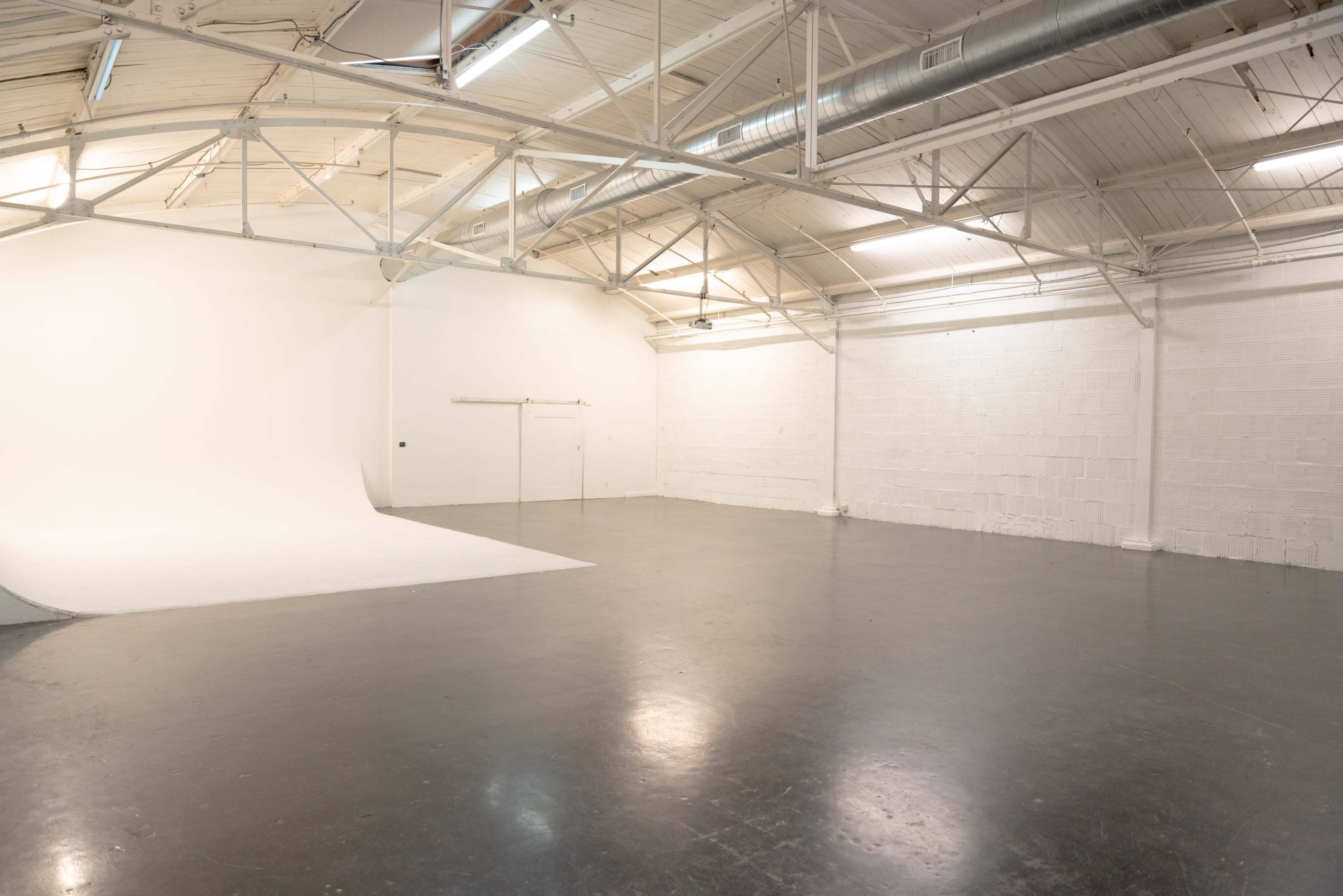 The image shows a spacious, empty studio with a white backdrop and a polished concrete floor.