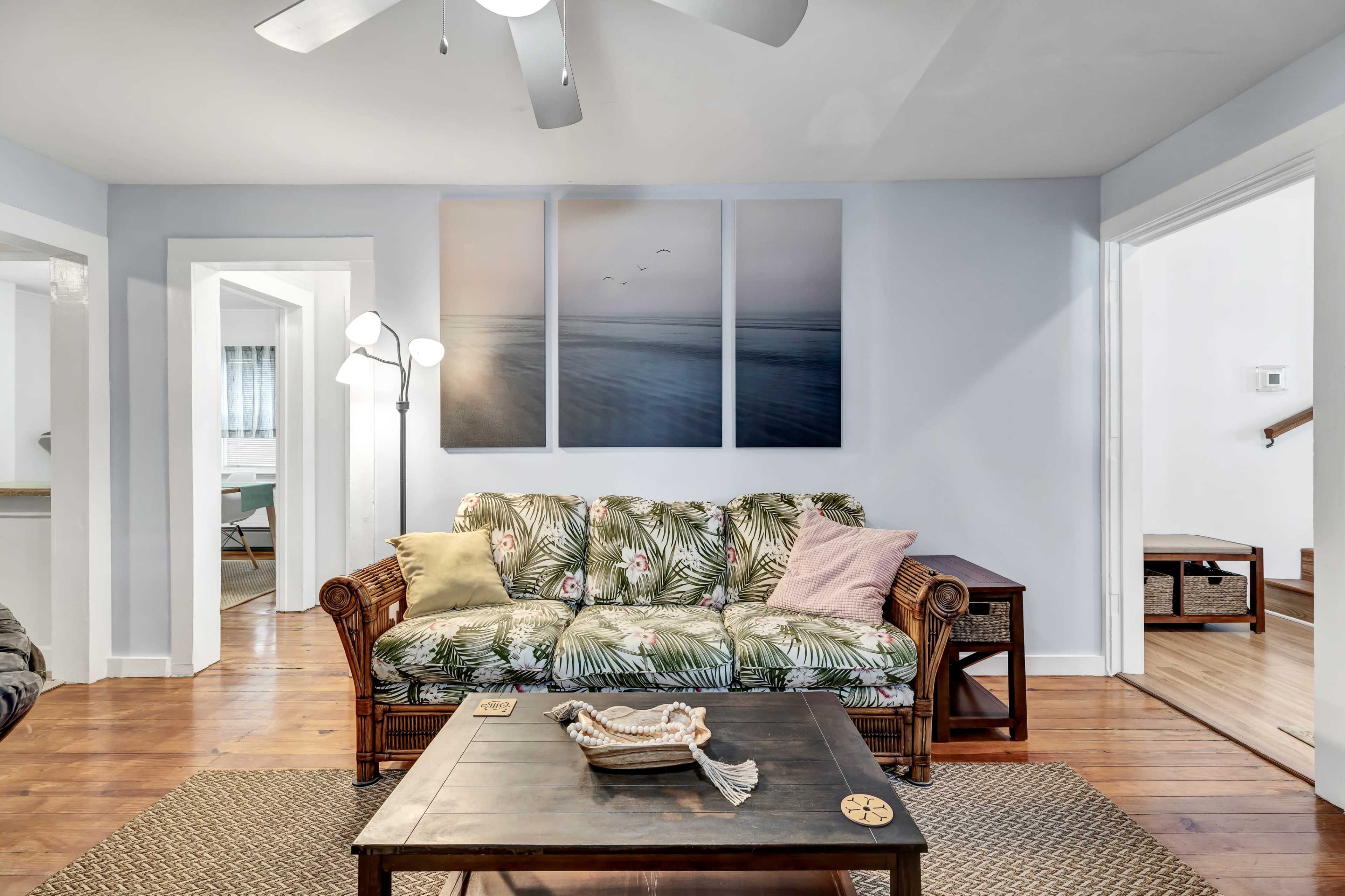 A living room features a tropical-themed couch, a wooden coffee table, and wall art depicting a serene seascape.
