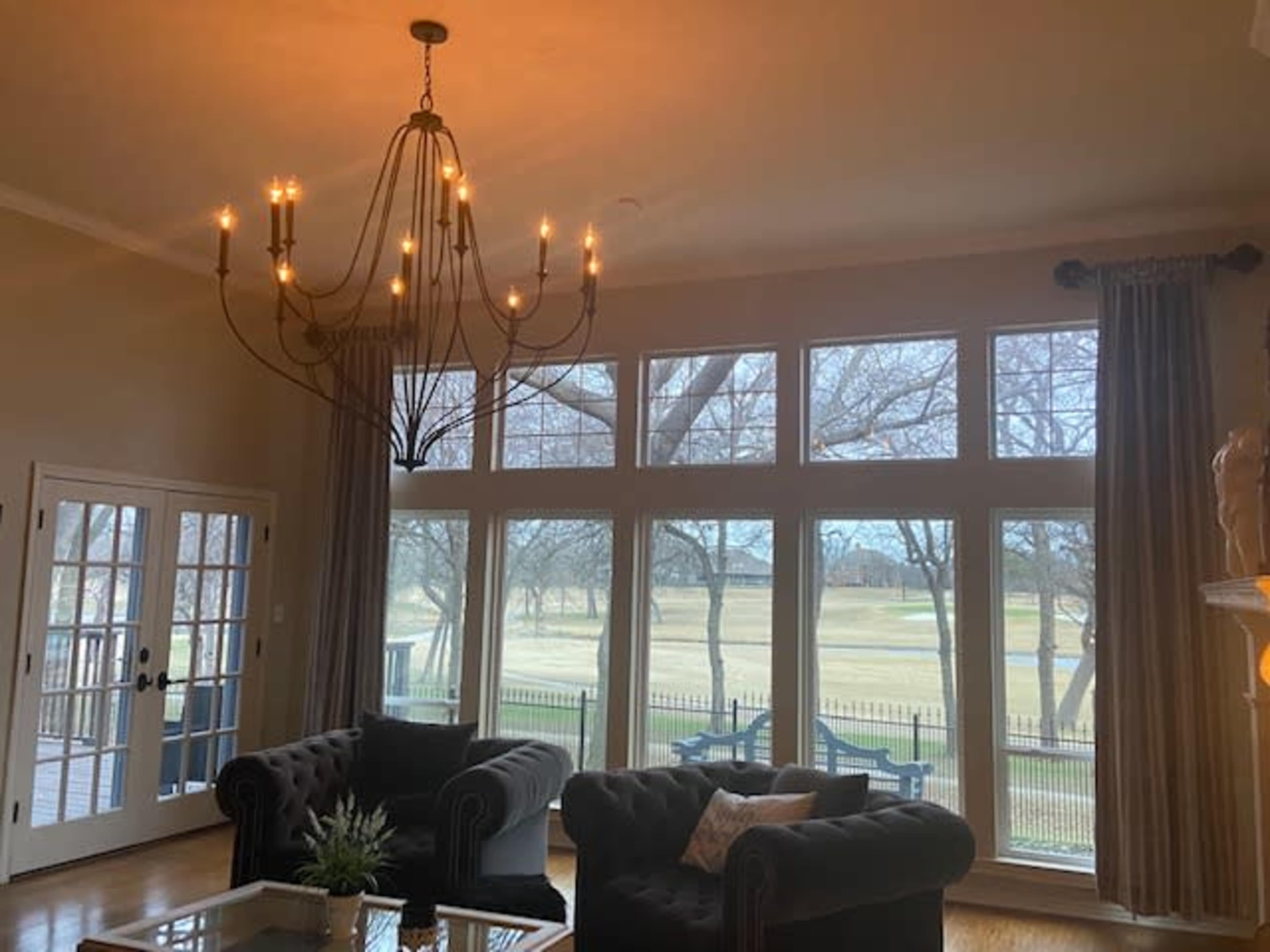 A spacious living room features a chandelier and large windows overlooking a landscape with trees and a golf course.