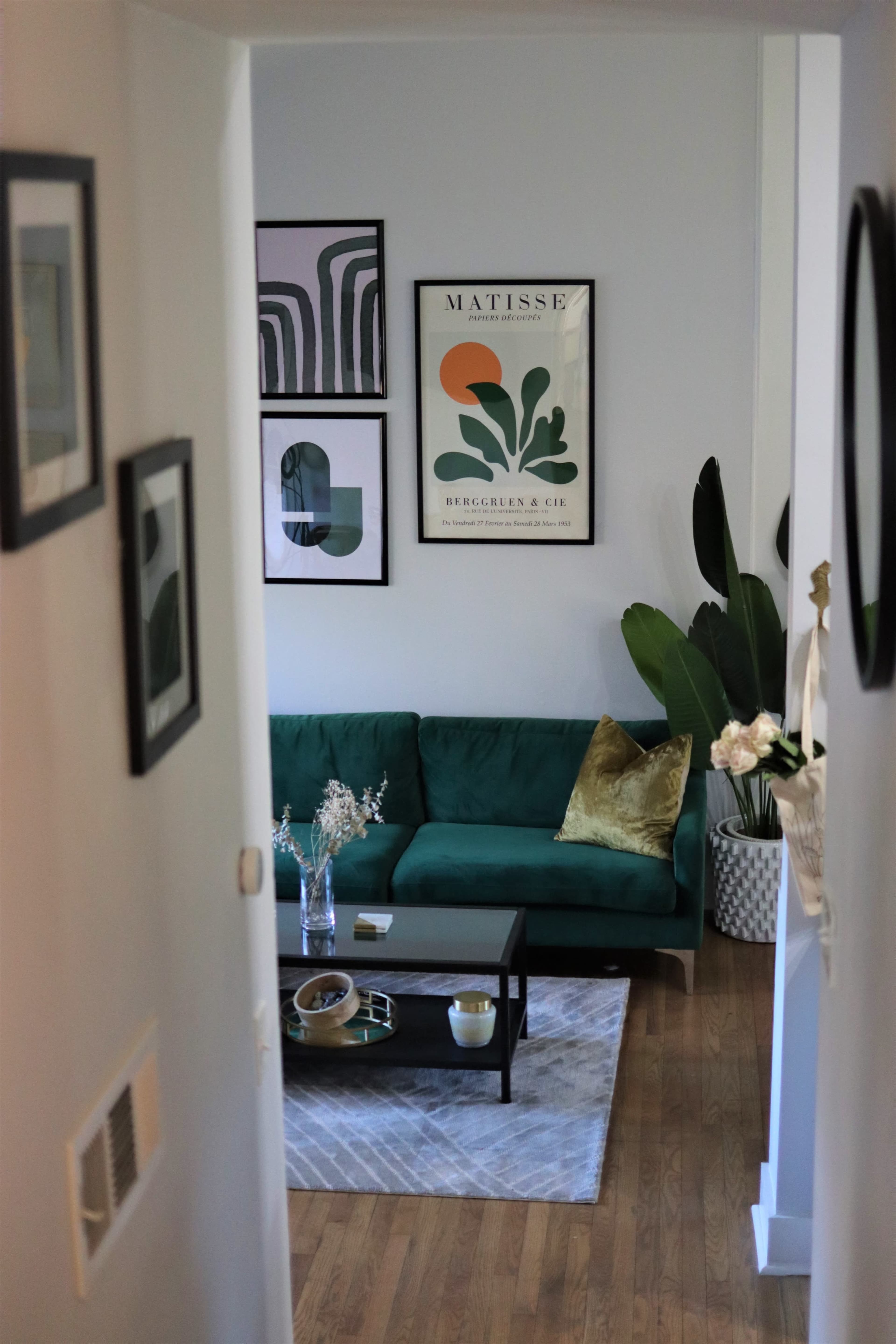 A green sofa with decorative pillows sits in a living room adorned with framed artwork and a coffee table, viewed from a staircase.
