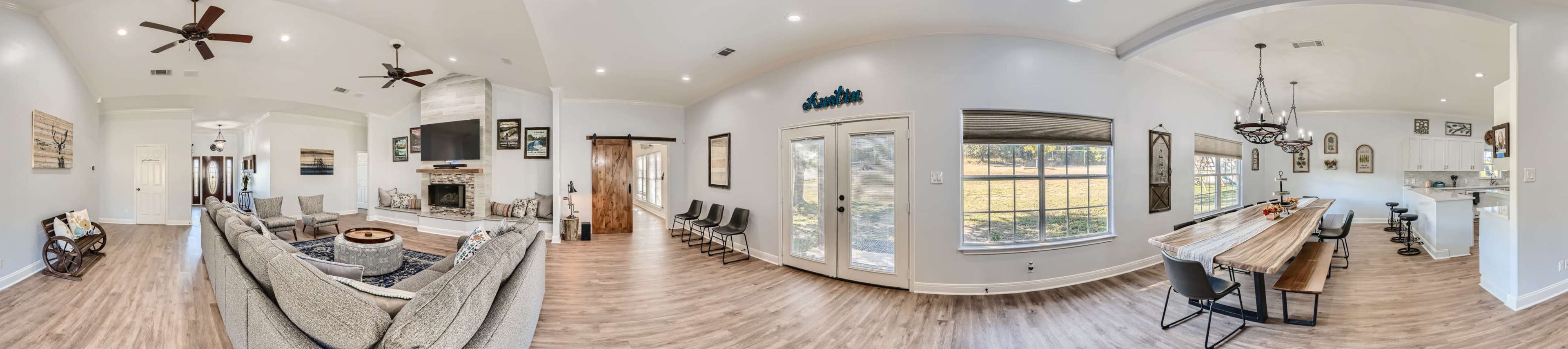 The image shows a spacious, open-concept living area and dining space with a central fireplace and large windows overlooking a yard.