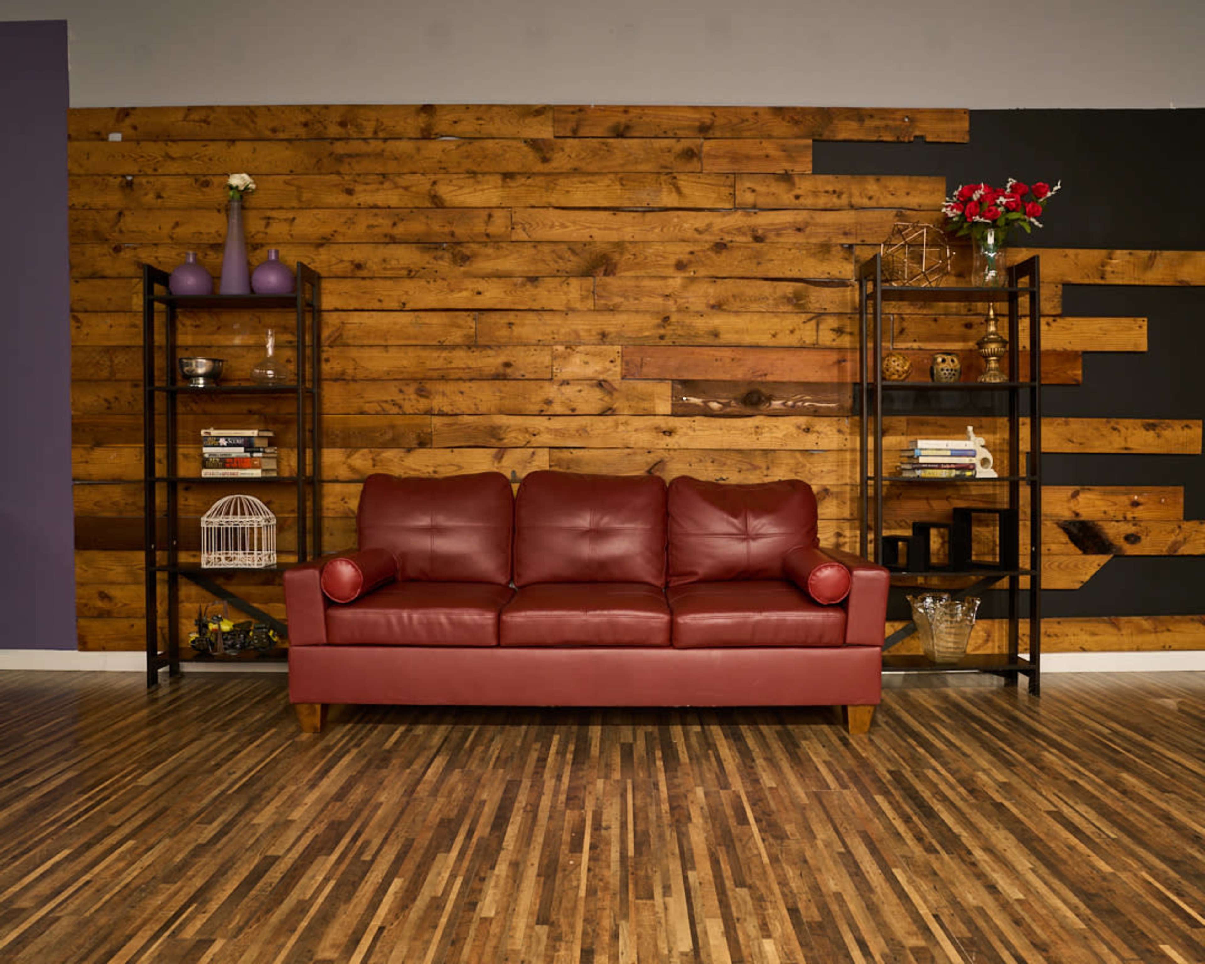 A red leather sofa is placed against a wooden-paneled wall, with black metal shelving units on either side displaying decorative items and books.