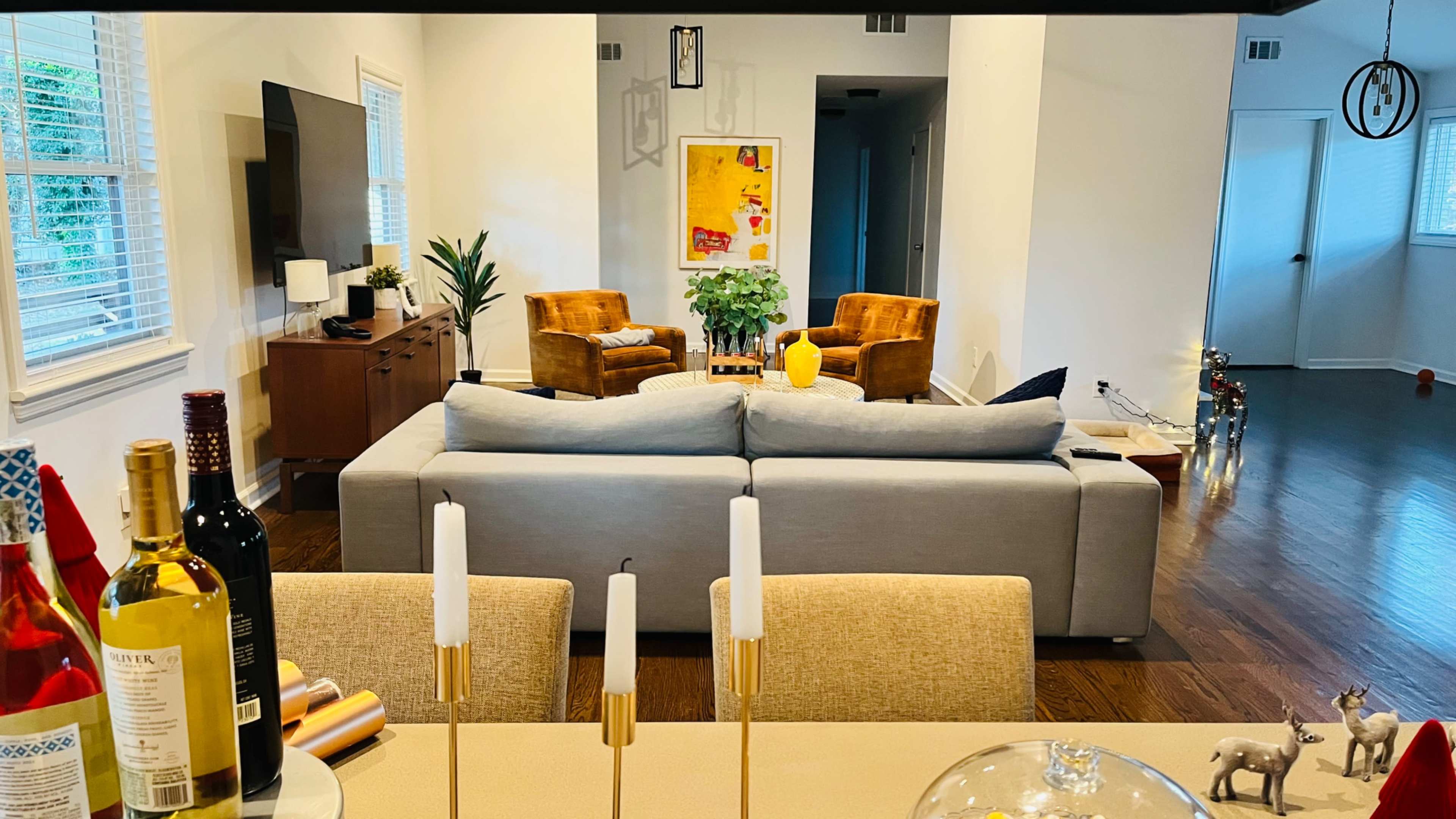 The image shows a modern living room with a gray sofa facing two armchairs, a wooden sideboard, and a dining table set in the foreground.
