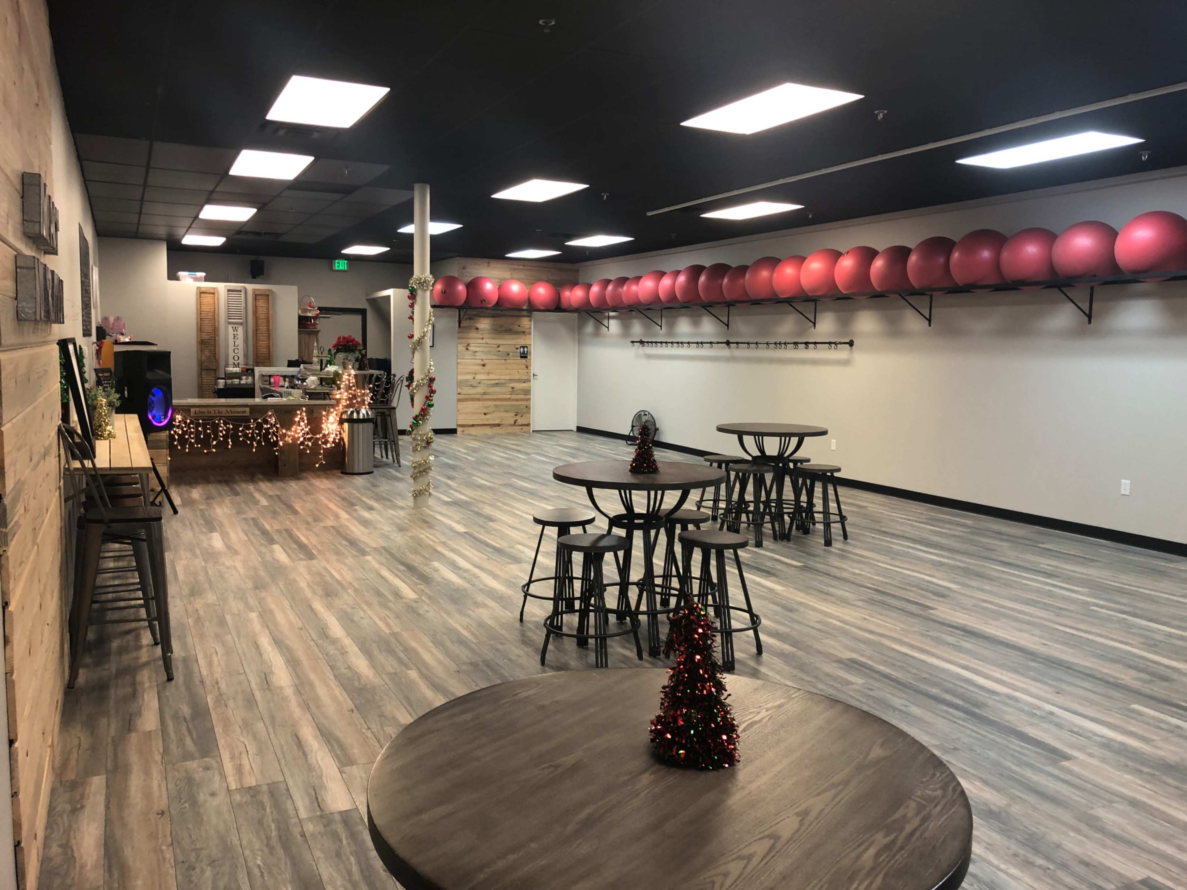 A spacious fitness studio with wooden flooring, several round tables, and a row of exercise balls along the back wall.